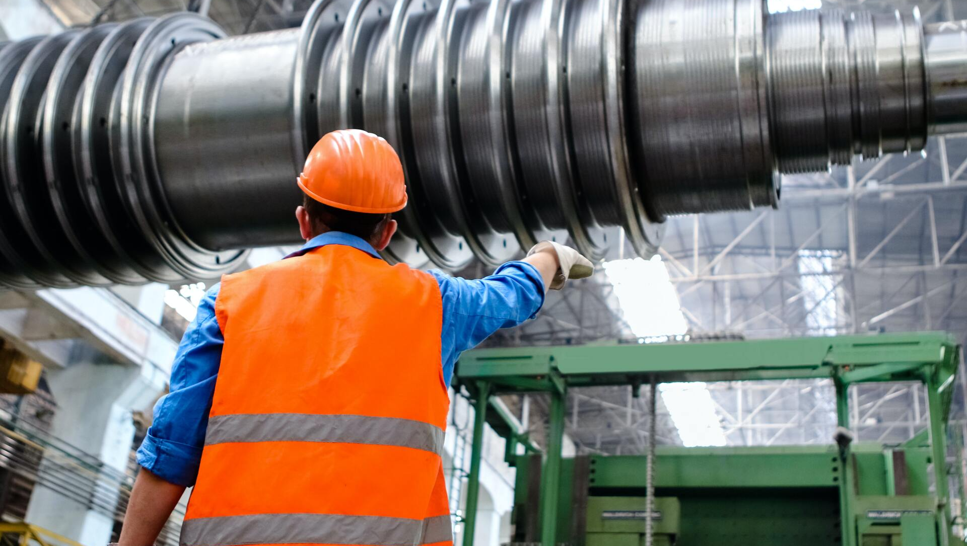 A man wearing an orange vest and hard hat is standing in front of a large metal pipe.