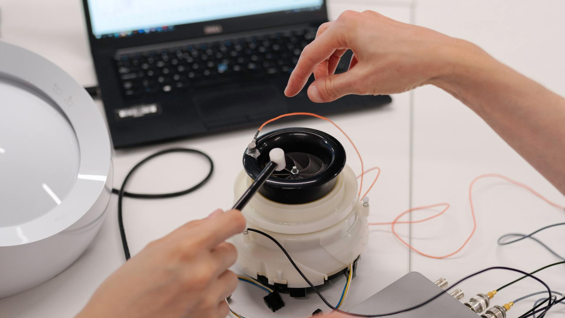 A person is working on a device with a laptop in the background.