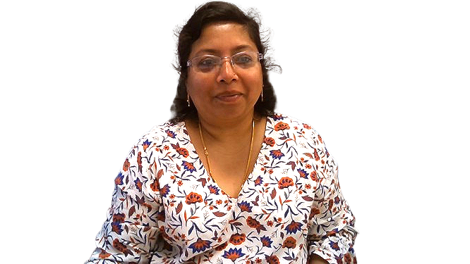 A woman wearing glasses and a floral shirt is standing in front of a white background.