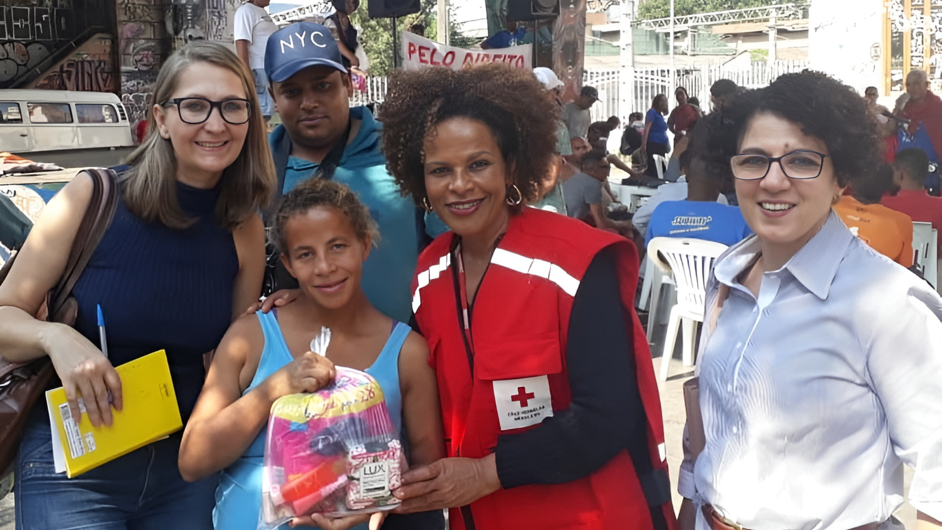 Um grupo de pessoas posa para uma foto com uma mulher de jaqueta vermelha com uma cruz.