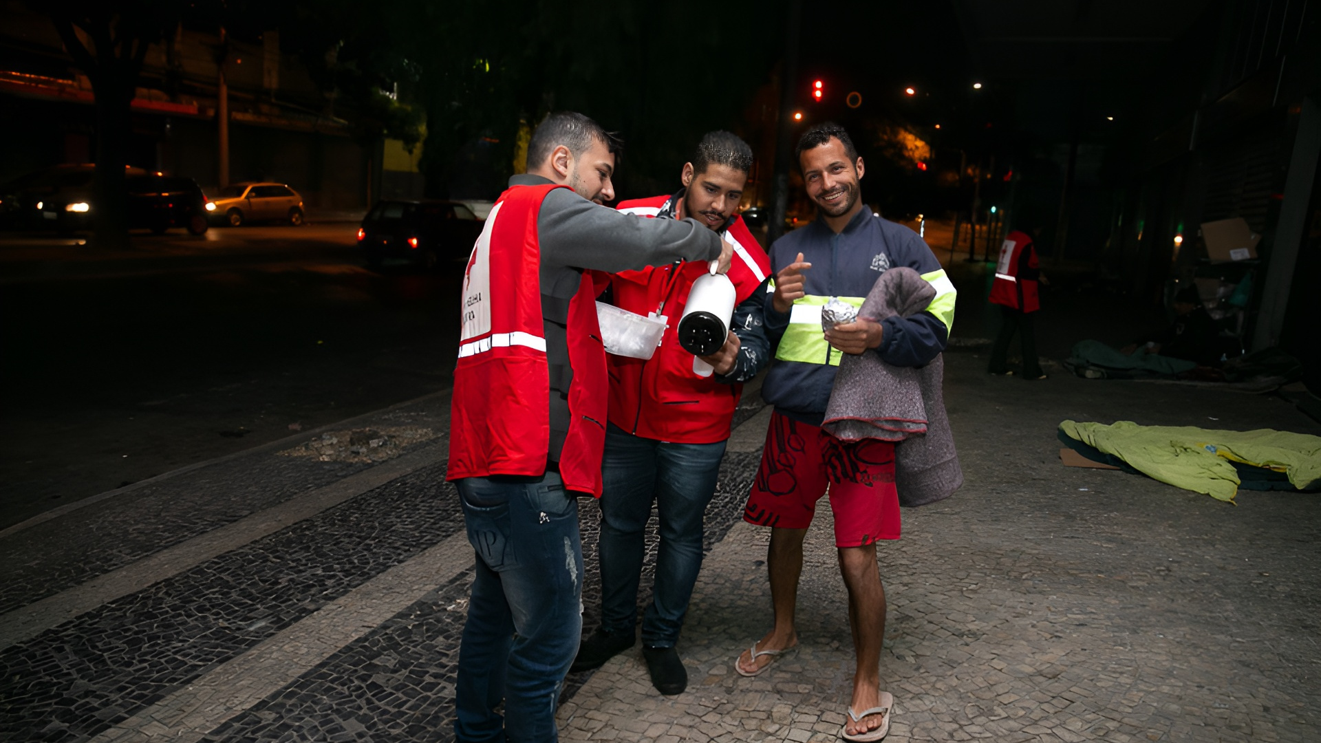 Um grupo de homens está parado um ao lado do outro em uma calçada à noite.
