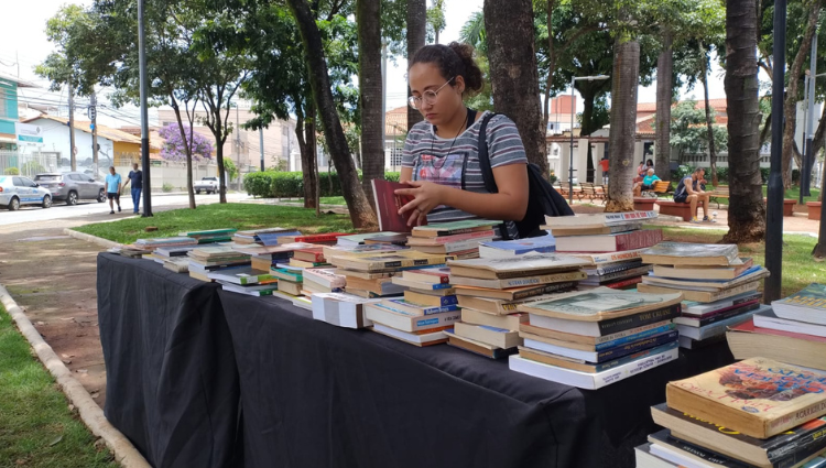 Uma mulher está diante de uma mesa cheia de livros.