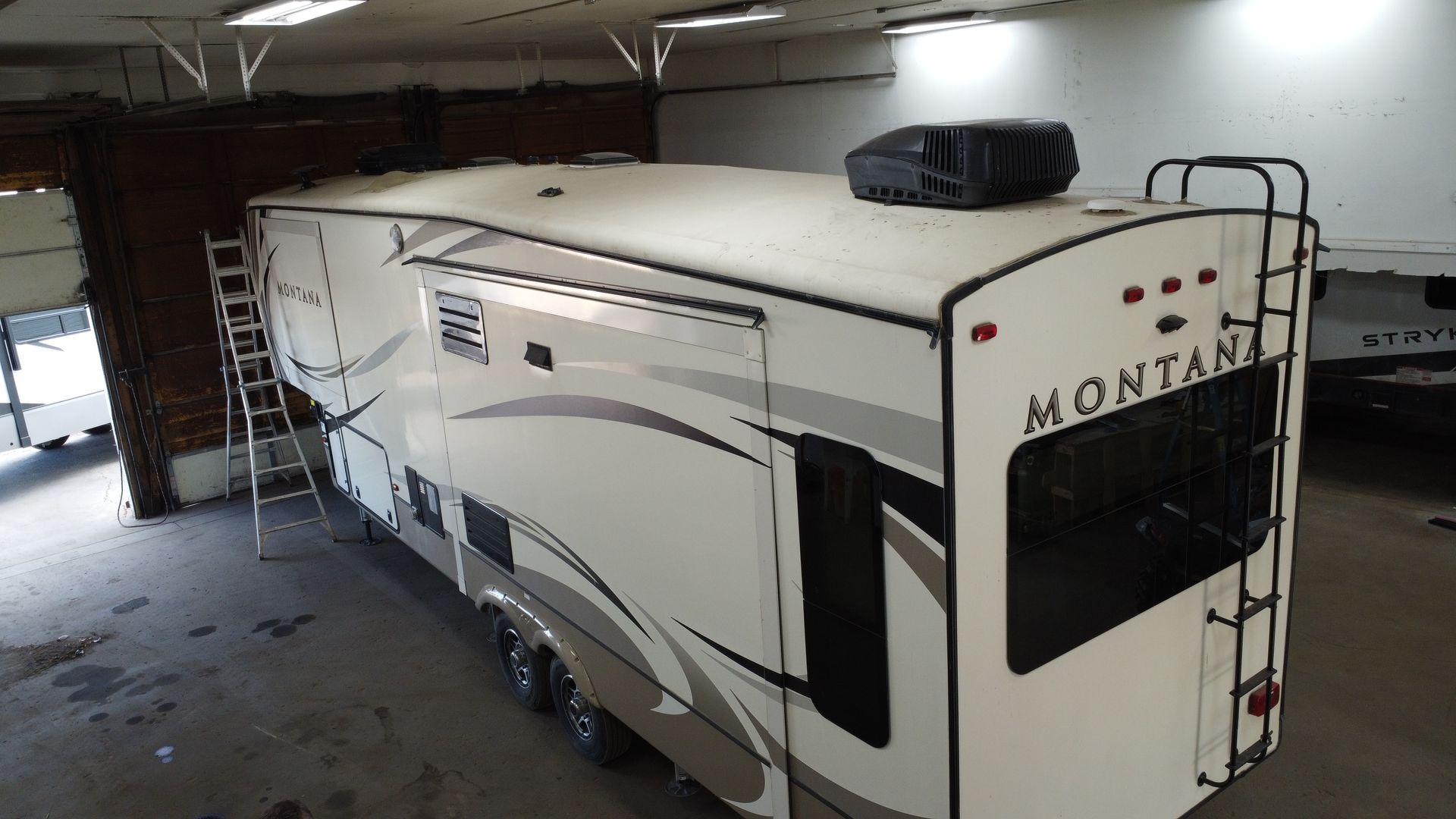 White Montana RV parked inside a building with a ladder against the side.
