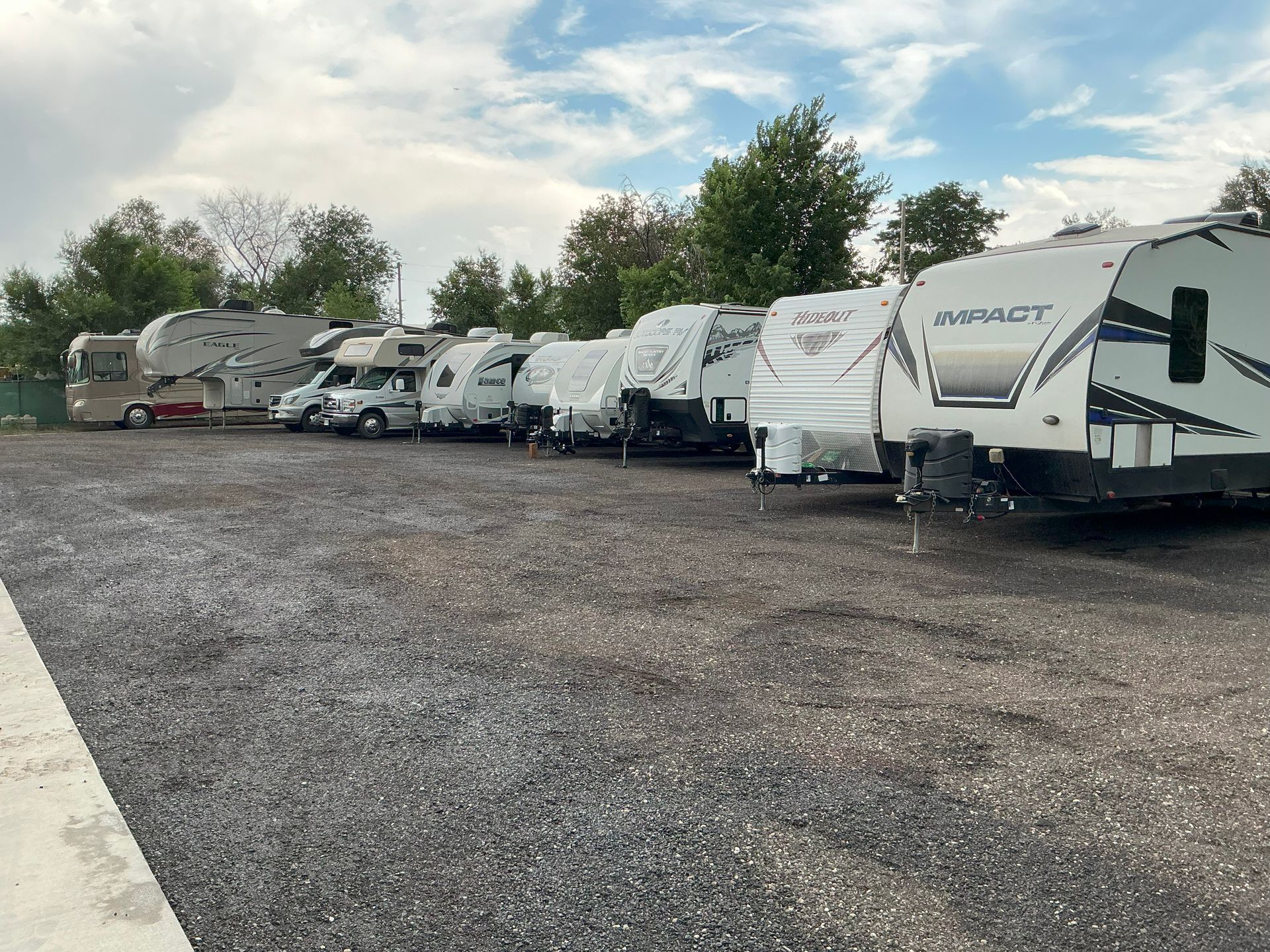RVs and campers parked on a gravel lot under a partly cloudy sky.