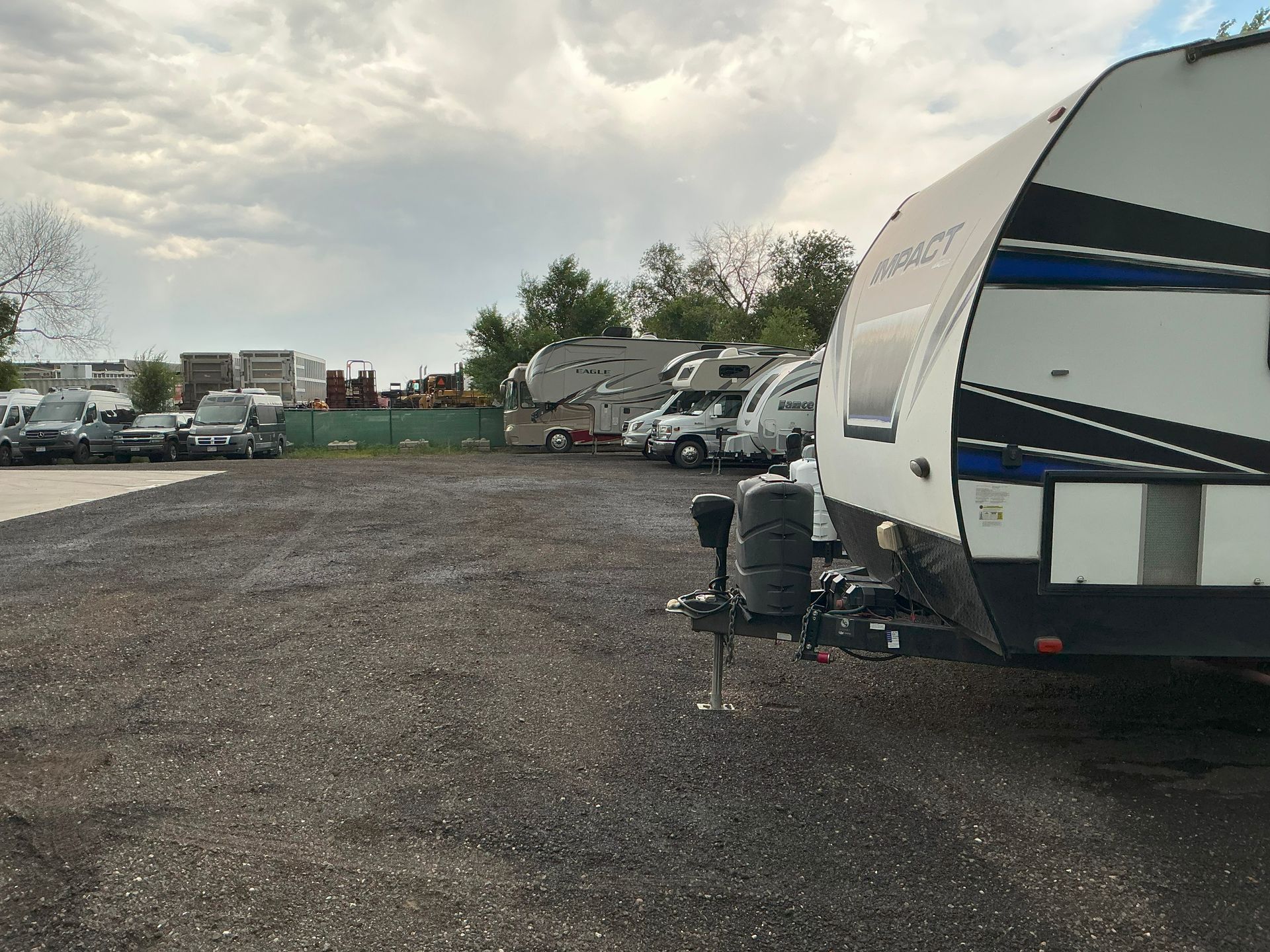 RVs and trucks parked on a gravel lot under a cloudy sky.