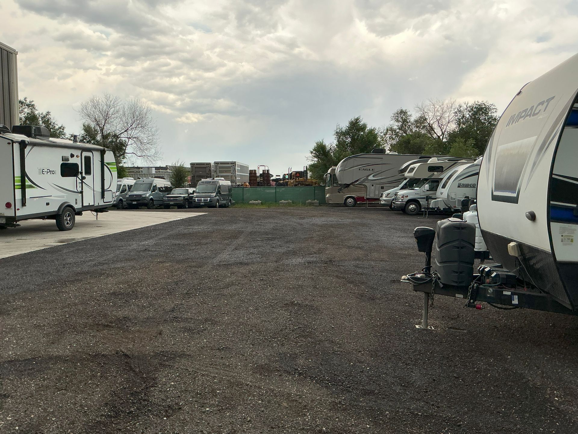 Gravel parking lot filled with RVs and cars under a cloudy sky.