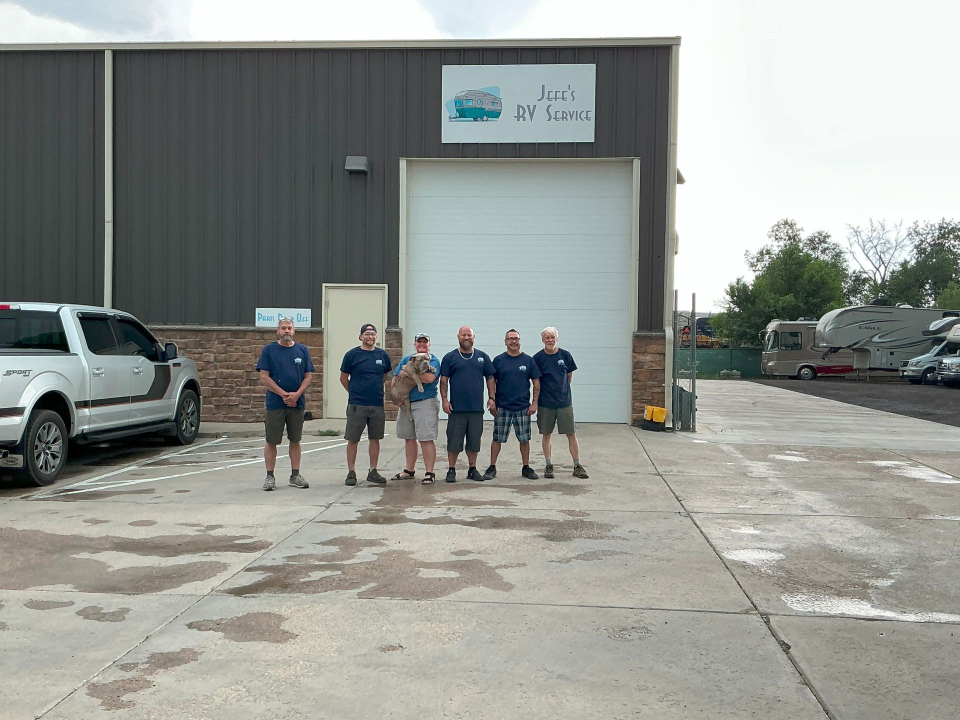 Group of men standing in front of a building with a garage door. A pickup truck is on the left.