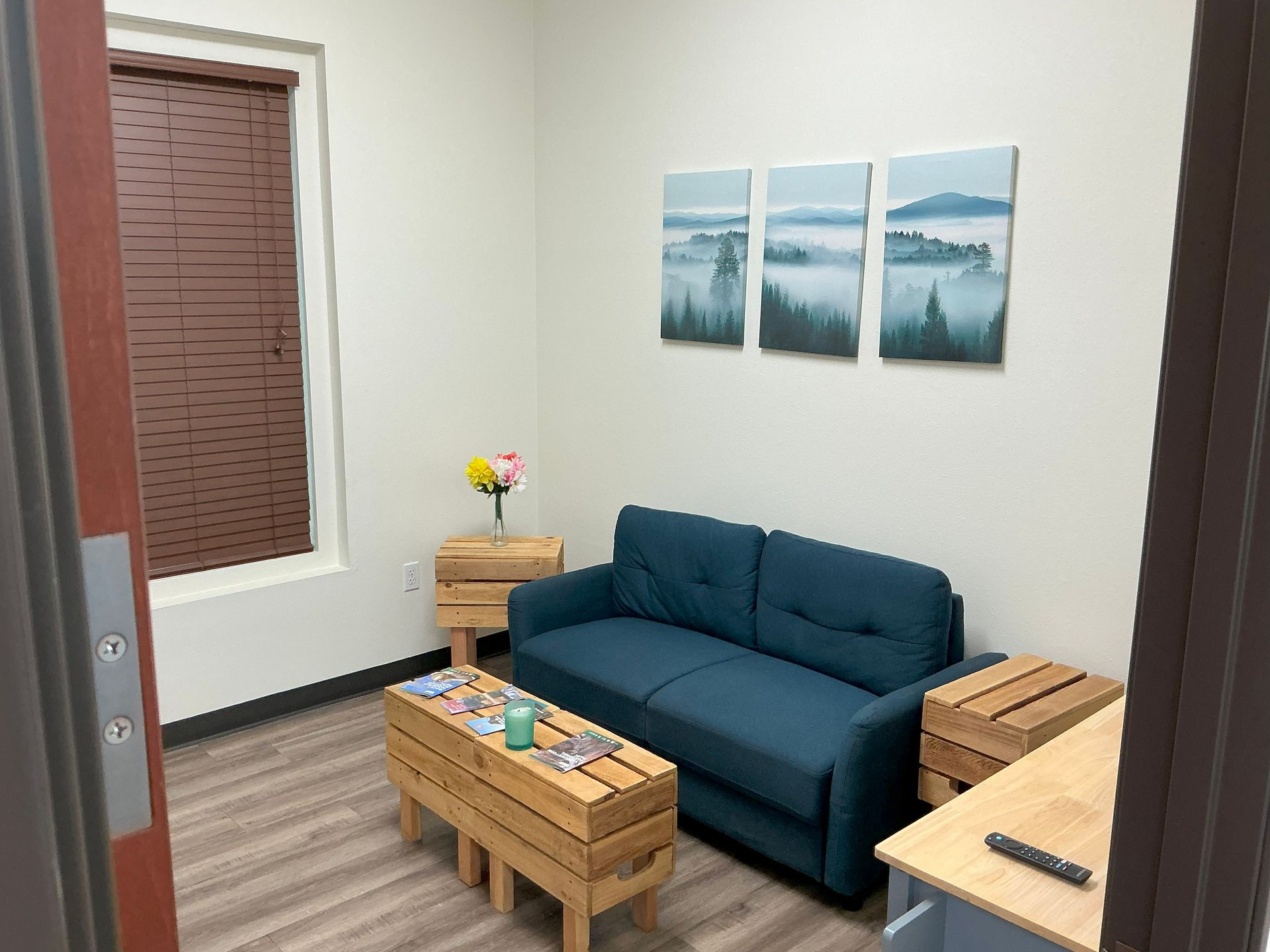 A small waiting room with teal sofa, wooden crates, and landscape art on the wall.
