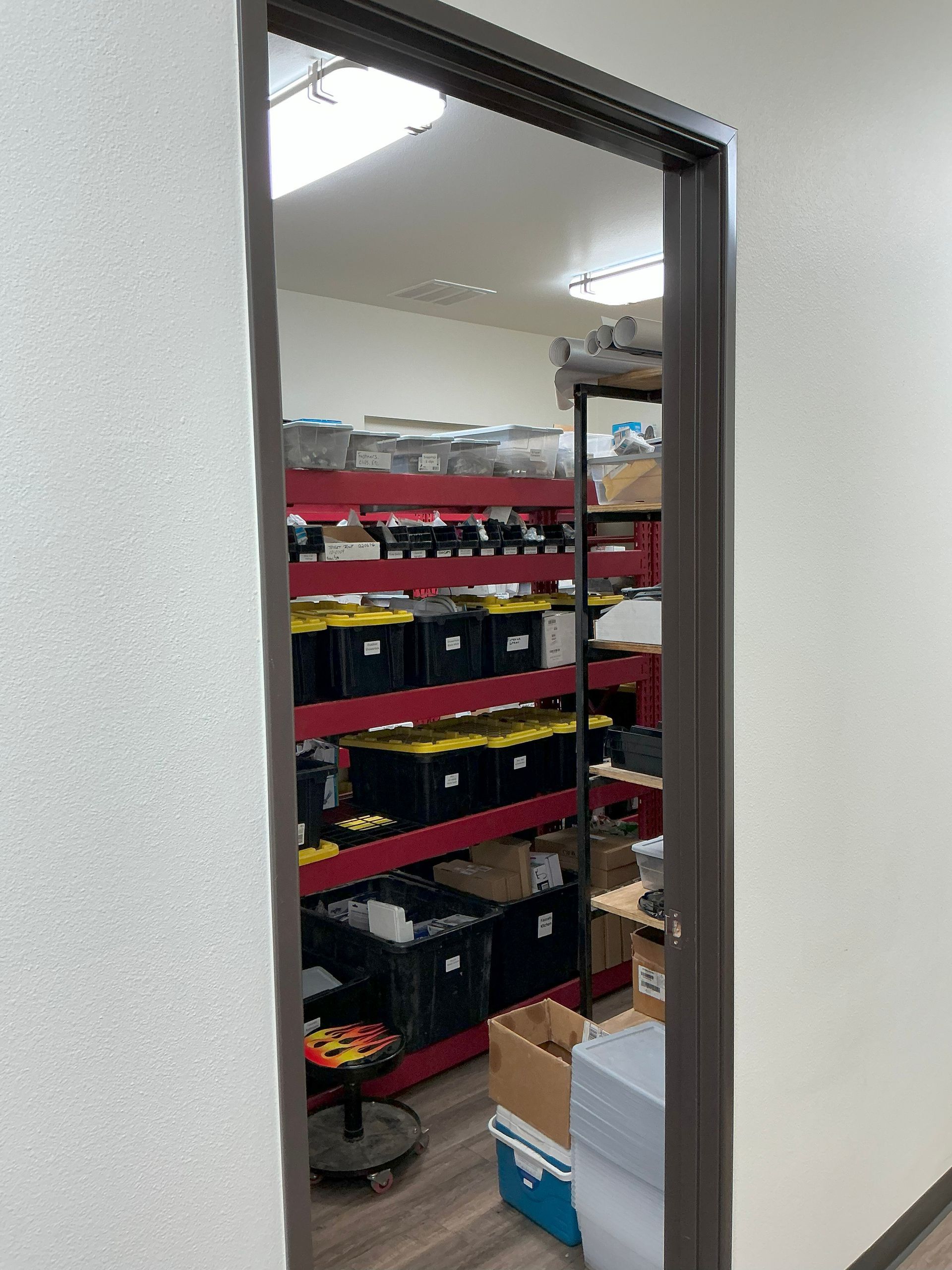 Doorway into a storage room with red shelving, black bins, and other supplies.