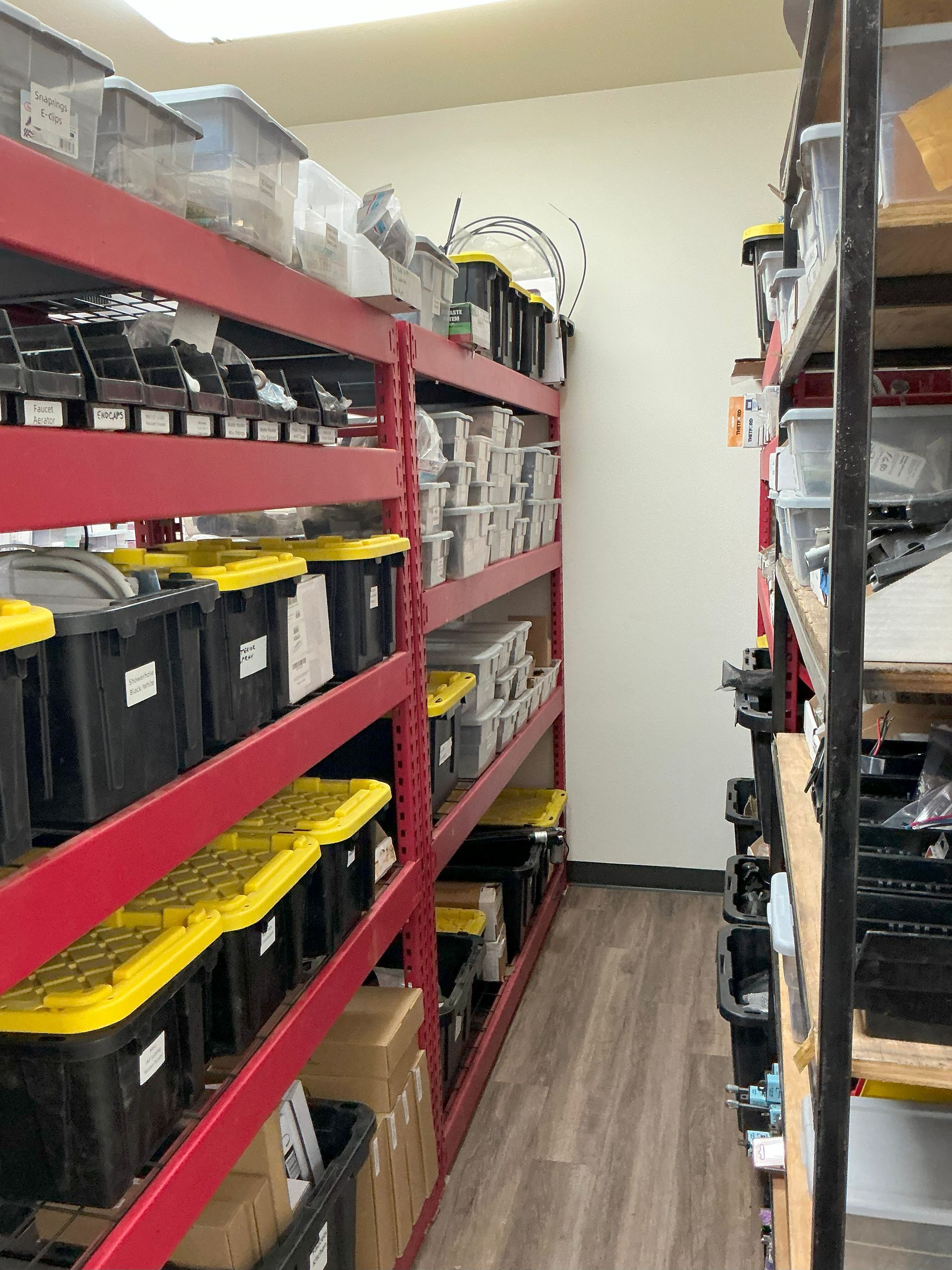 Red metal shelves filled with black bins and boxes in a storage room.