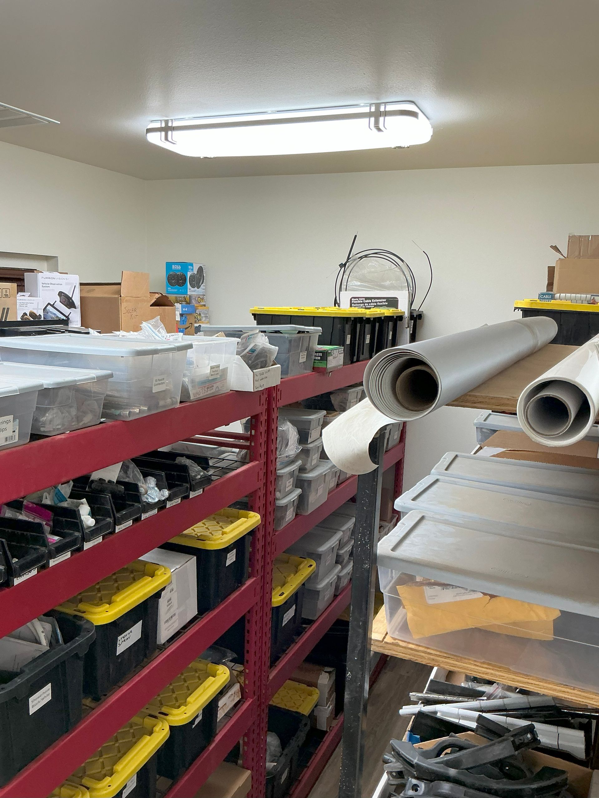 Shelves of parts and supplies in storage. Red shelves, yellow bins, tools, and a bright light.