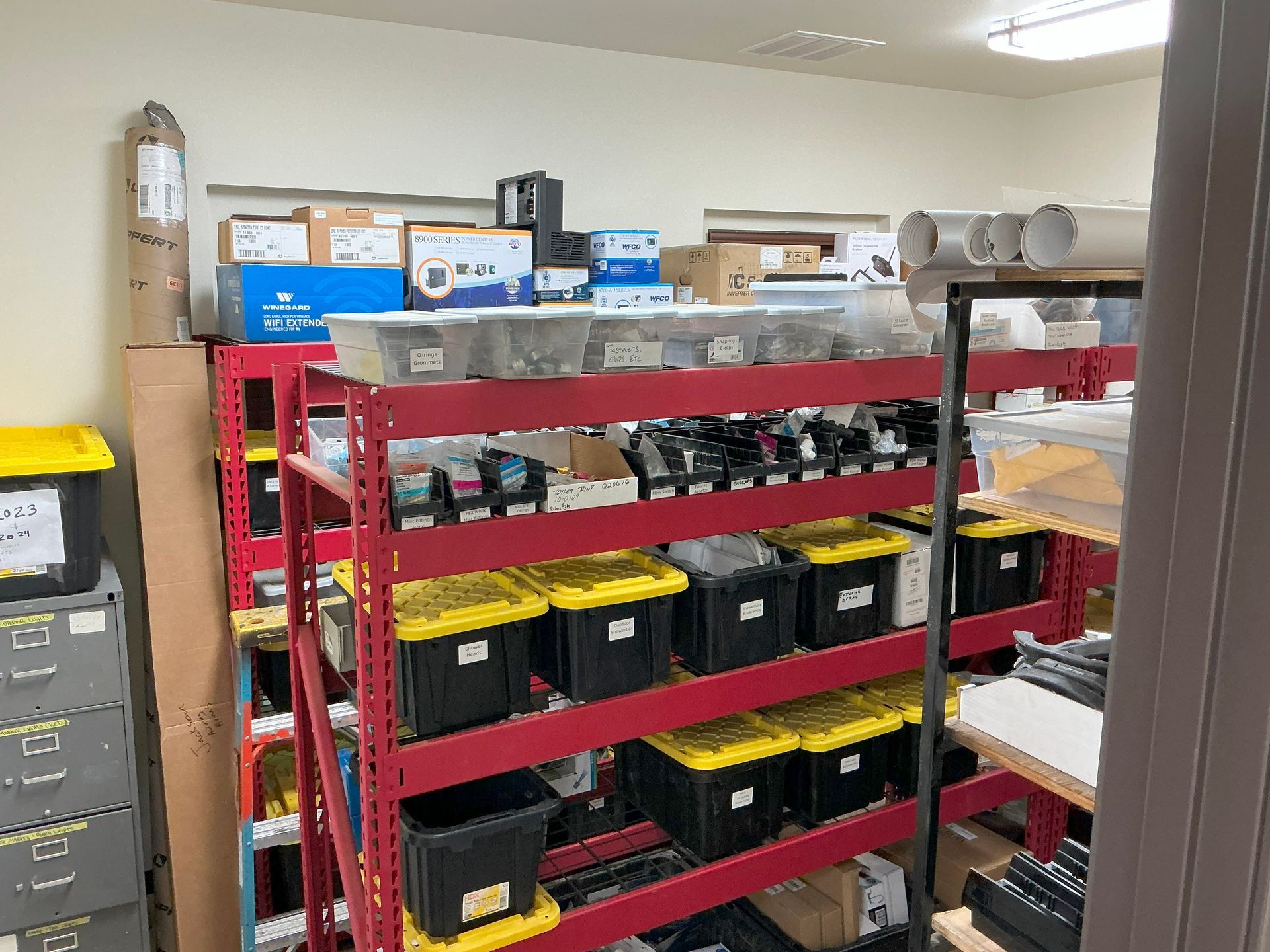 Red shelves filled with boxes, bins, and supplies in a storage room.