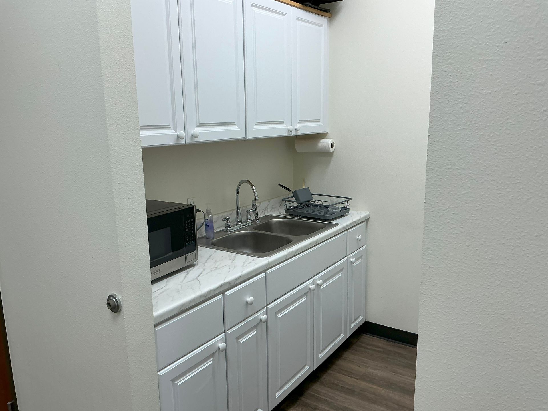 Small white kitchenette with microwave, sink, and cabinets.