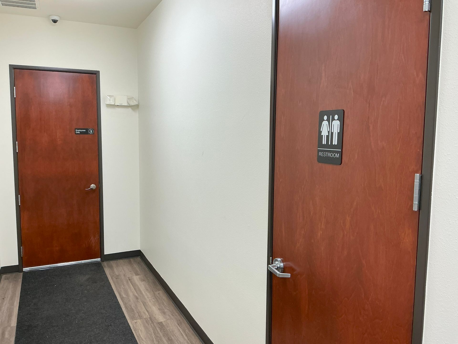 Hallway with two wooden doors, one marked as restroom, and a dark floor runner.
