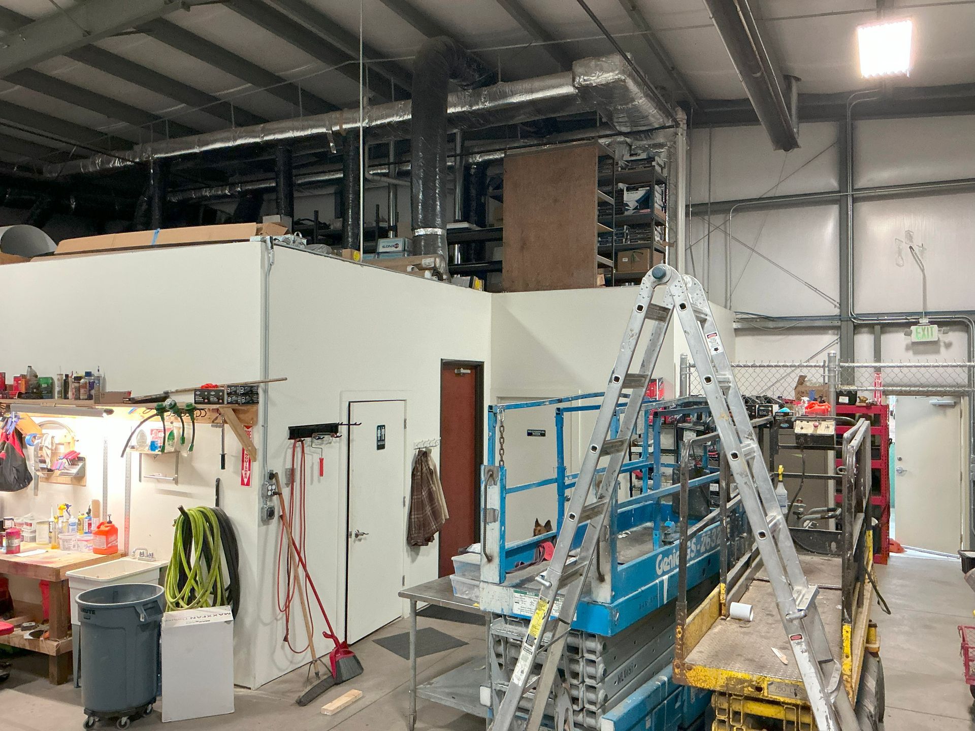 Interior of a workshop with walls, doors, shelves, a scissor lift, and a ladder.