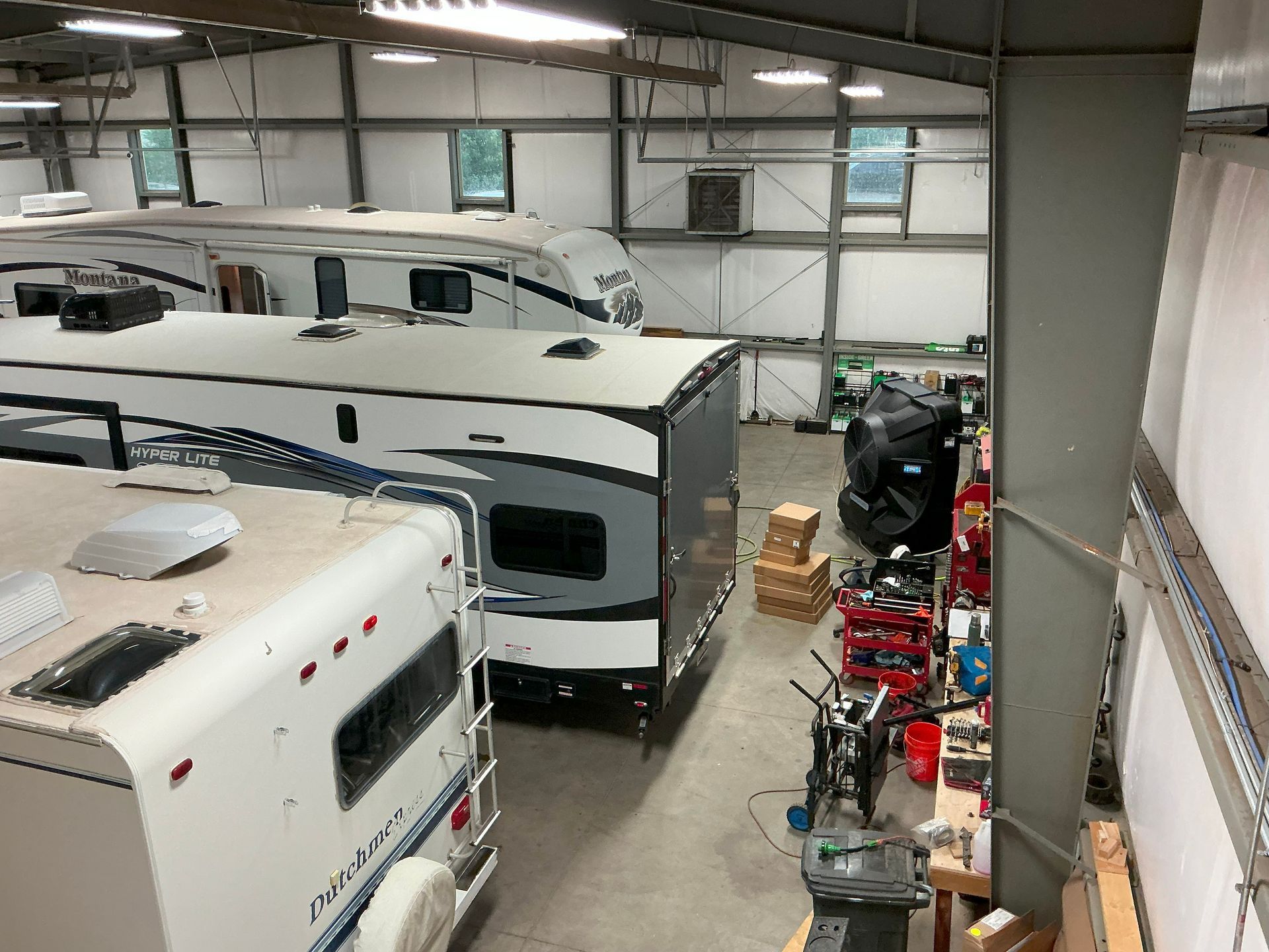 RVs inside a large warehouse. Various models are parked, with tools and equipment visible on the side.