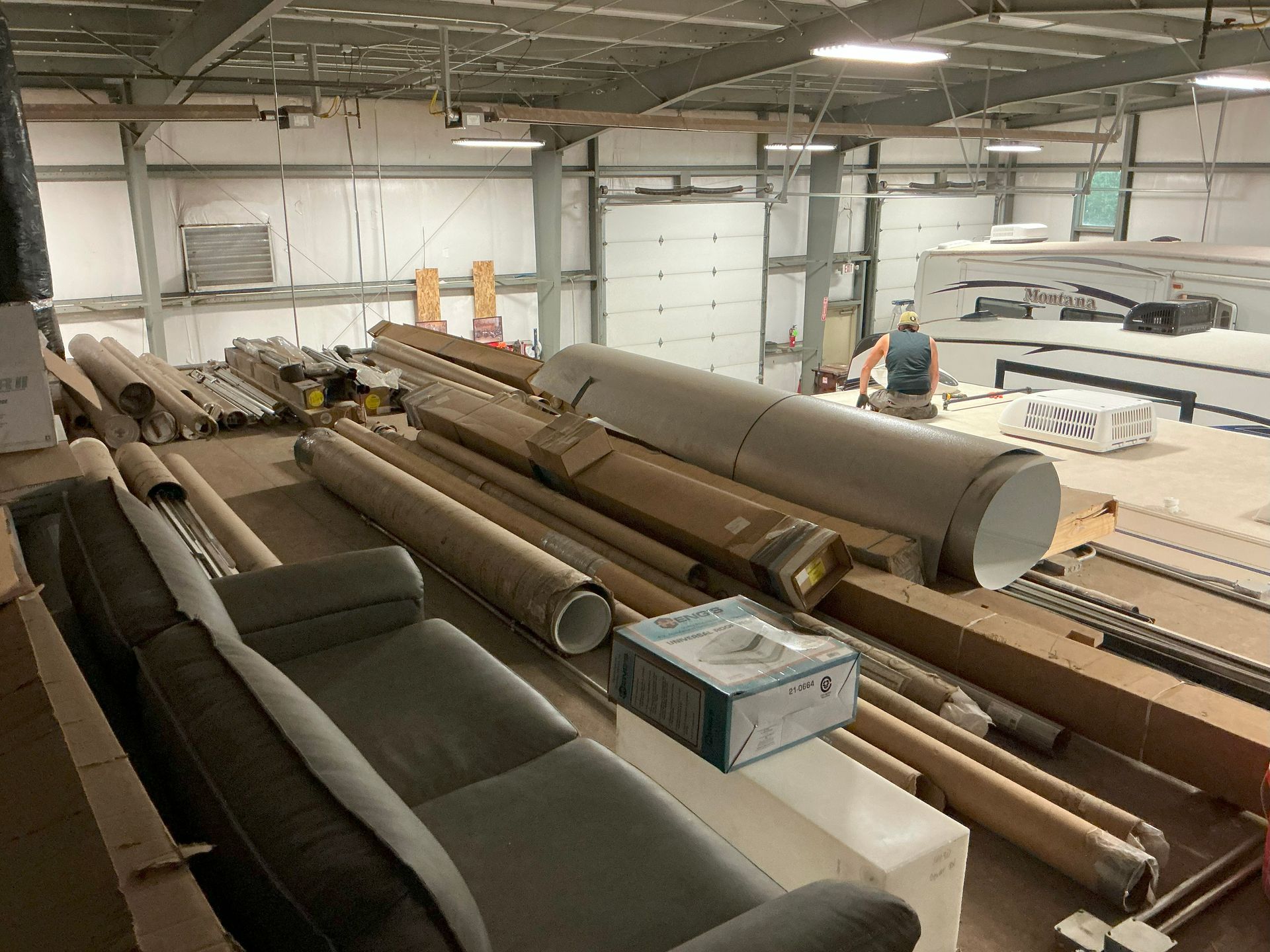 Warehouse interior with piles of cylindrical materials, a person working, and a gray couch.