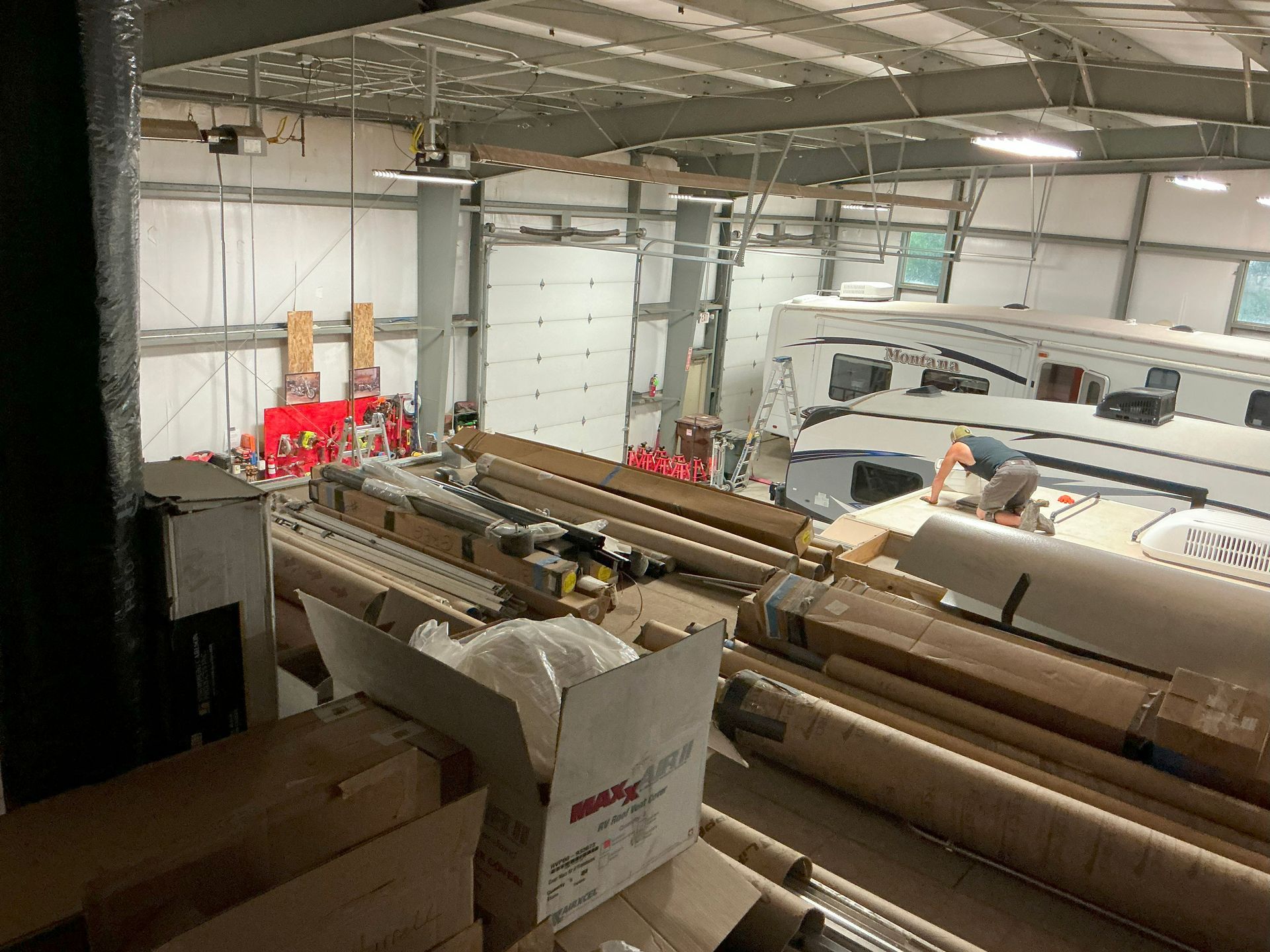 Warehouse interior with RVs, rolls of material, and boxes, possibly for repairs.