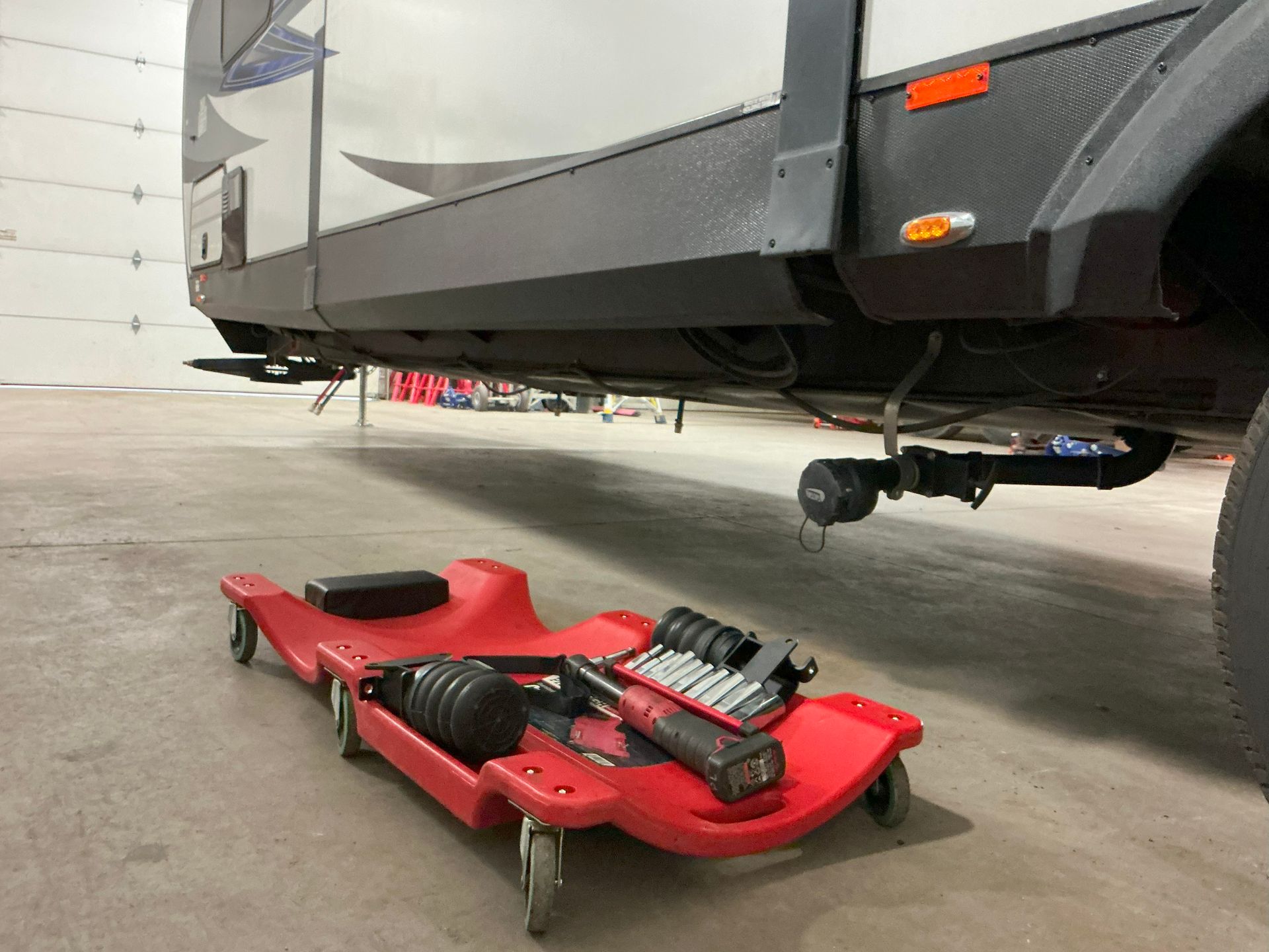 Red creeper with tools under an RV, likely for repairs in a garage.