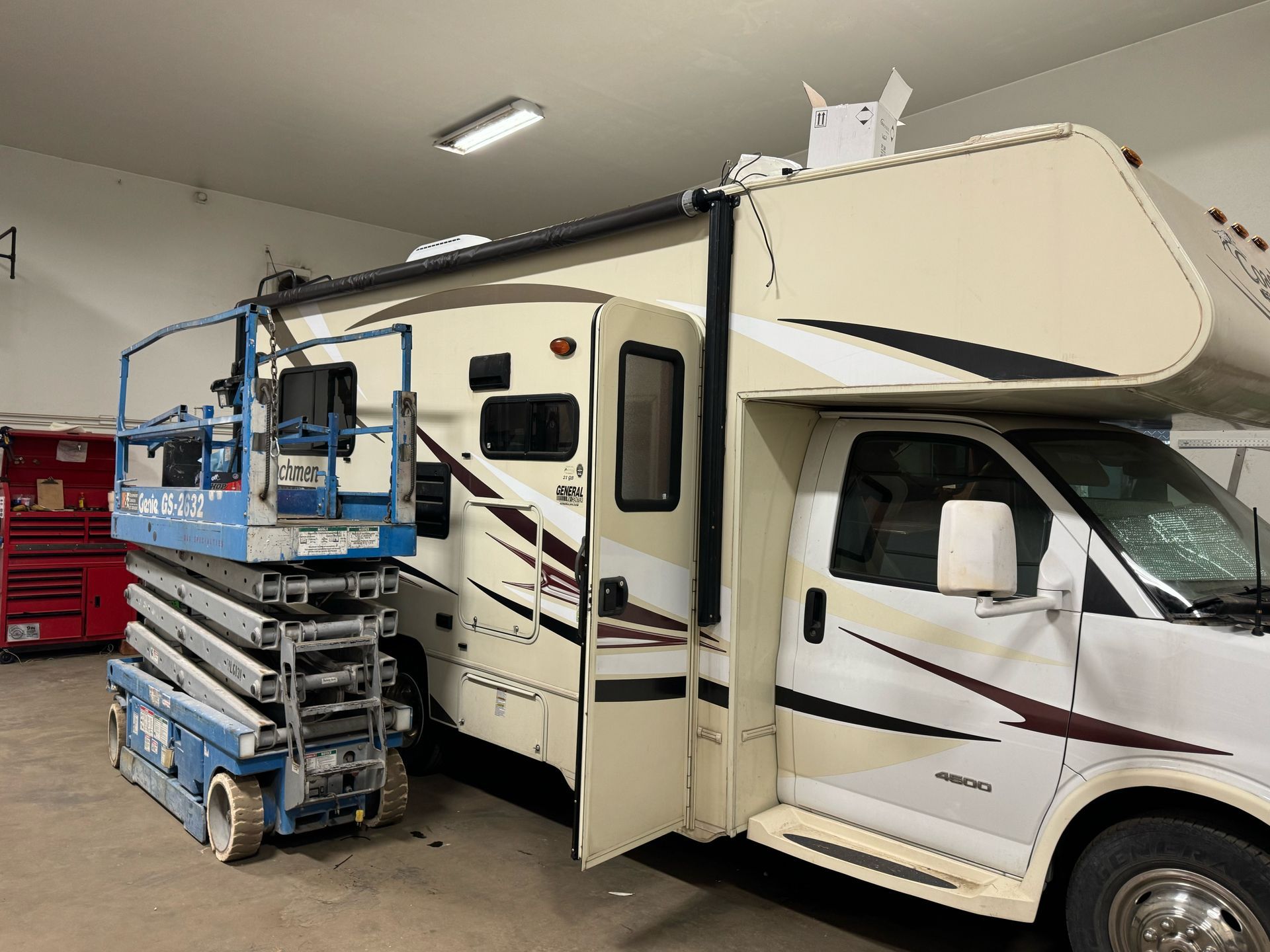 An RV parked inside a garage has a scissor lift next to it.