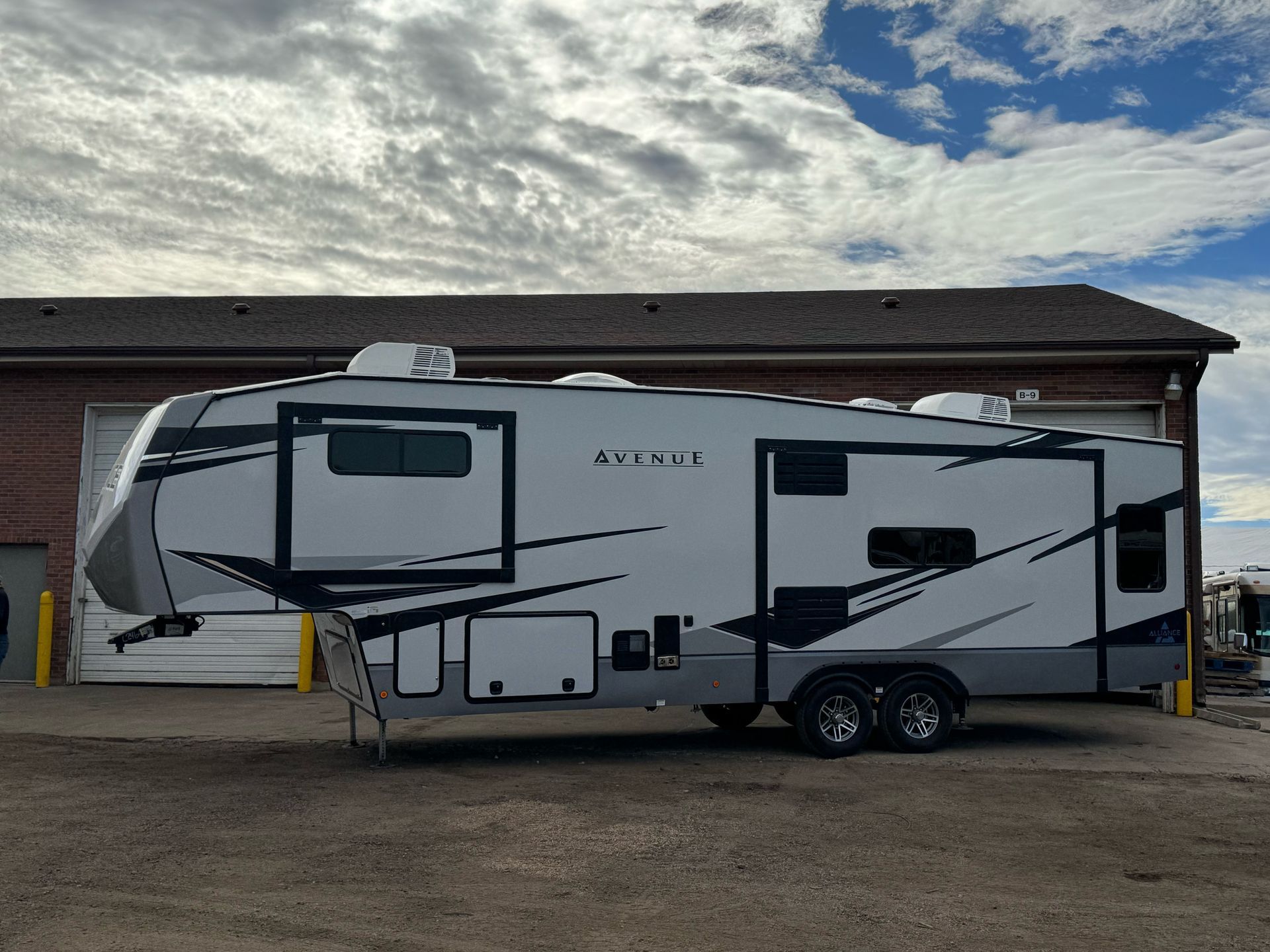 Gray and black RV parked outside a building, cloudy sky above.