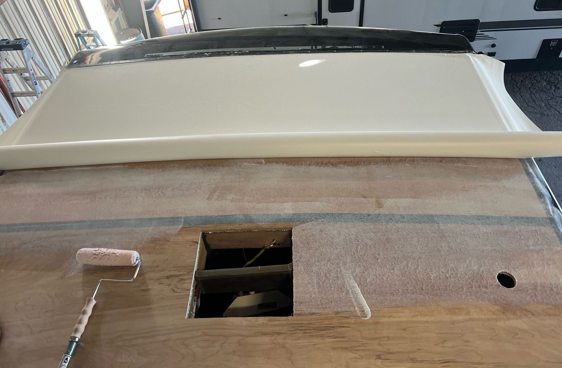 Wooden surface with a rectangular opening, a white trim piece, and a portion of a vehicle visible above.