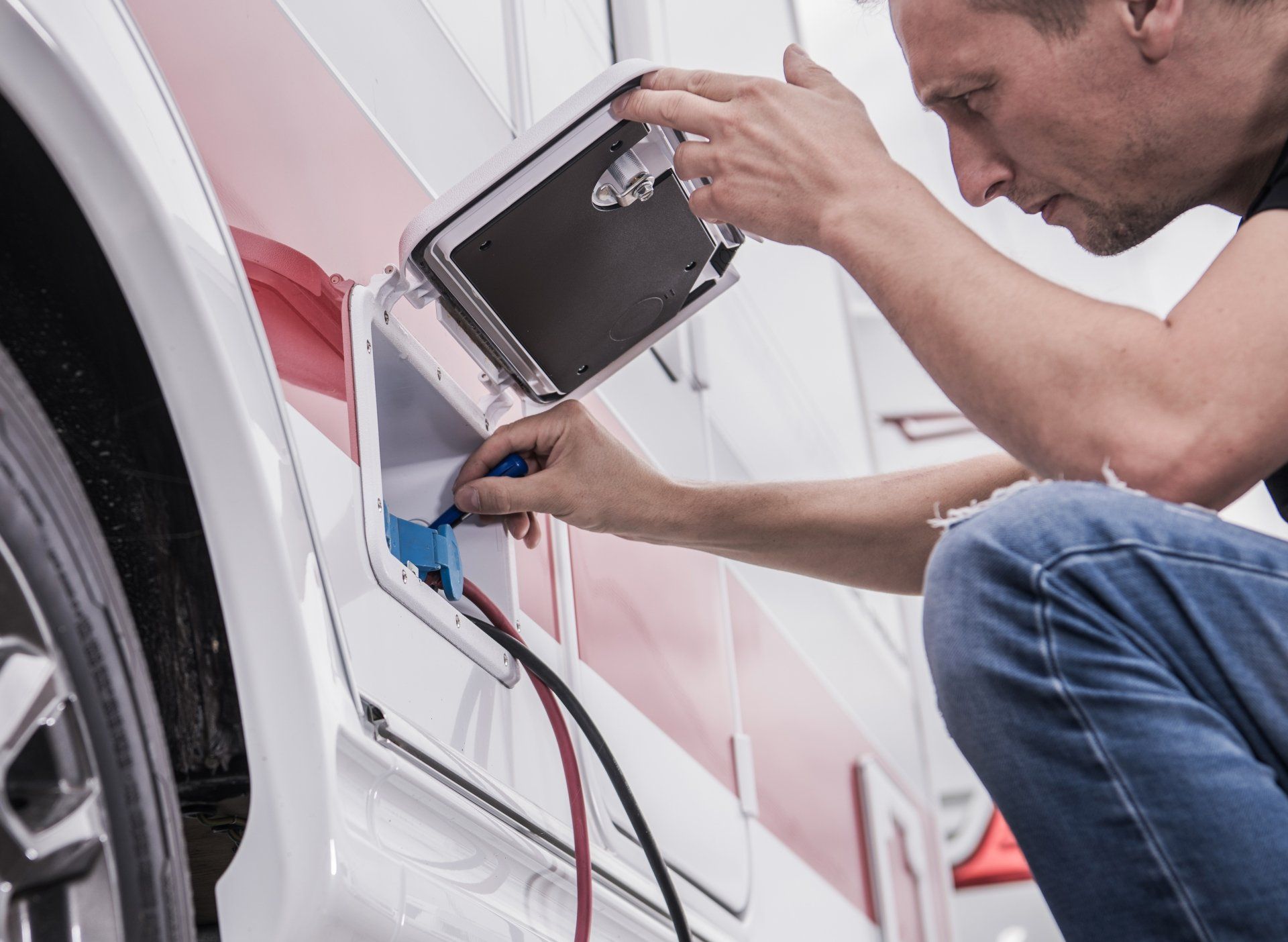 Man plugs power cord into an RV, outdoors. White RV with red trim, blue power outlet.
