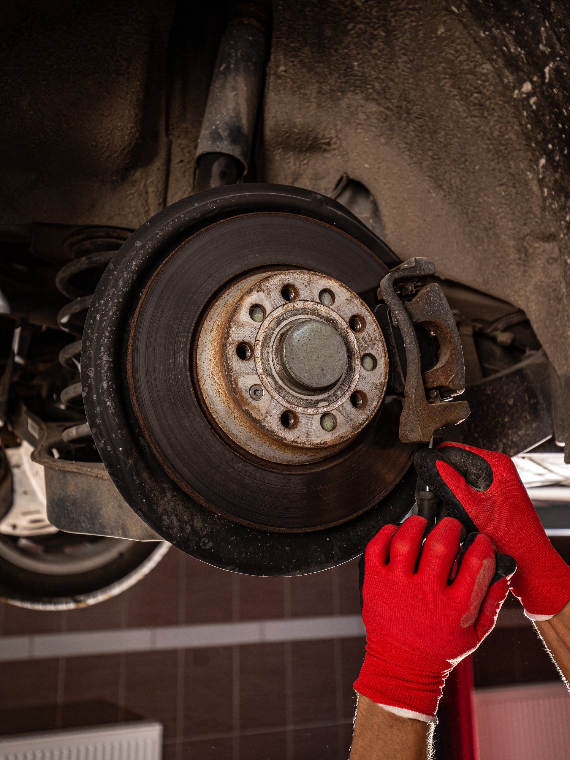 Mechanic in red gloves working on a car's brake rotor, inside a garage.