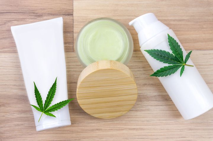 Cannabis skincare products on a wooden table: tubes, jars, and leaf logos