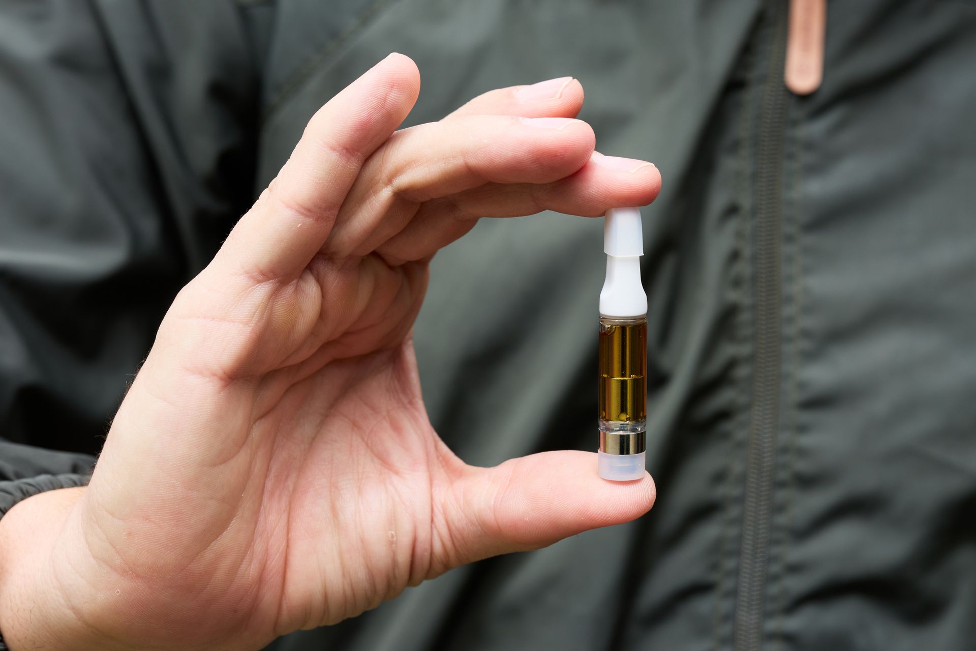 Hand holding a small amber vial with a white dropper, against a dark jacket background