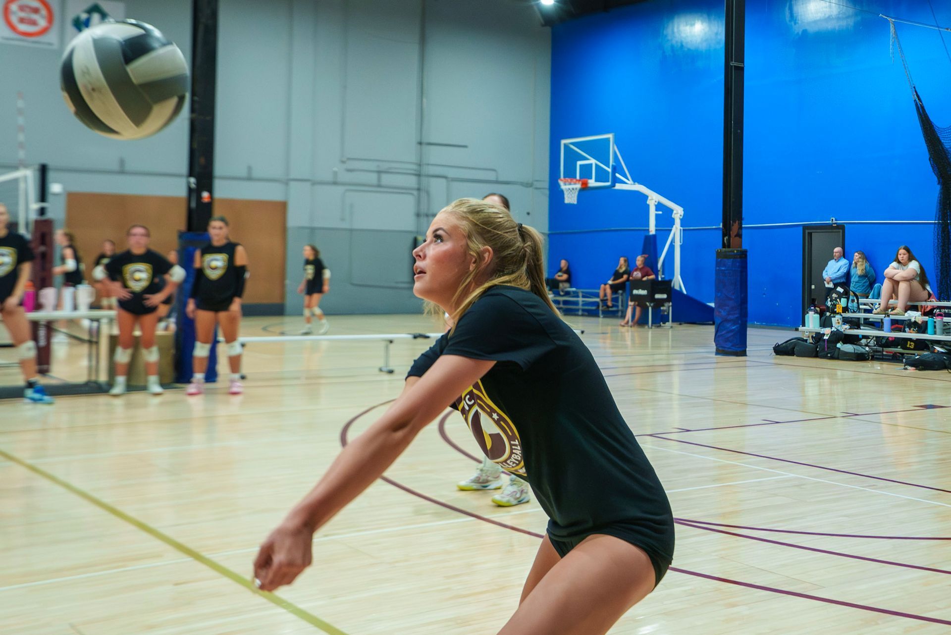 Girls, some carrying others piggyback style, pose with volleyballs in a gym, smiling.