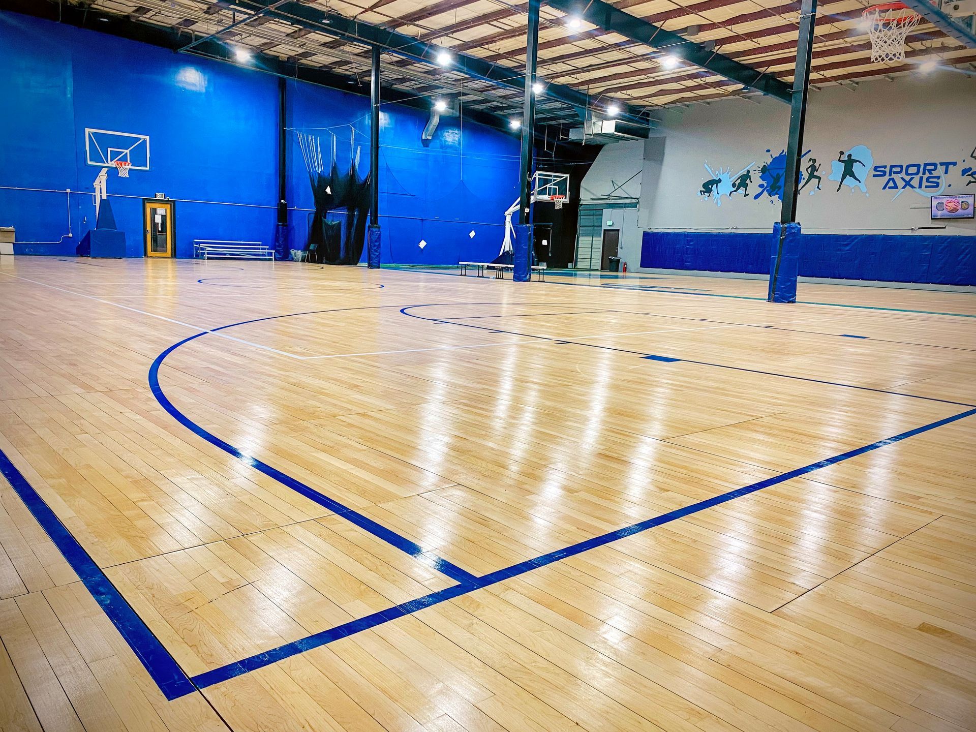 Indoor basketball court with wood floor, blue lines, blue walls, and hoops.