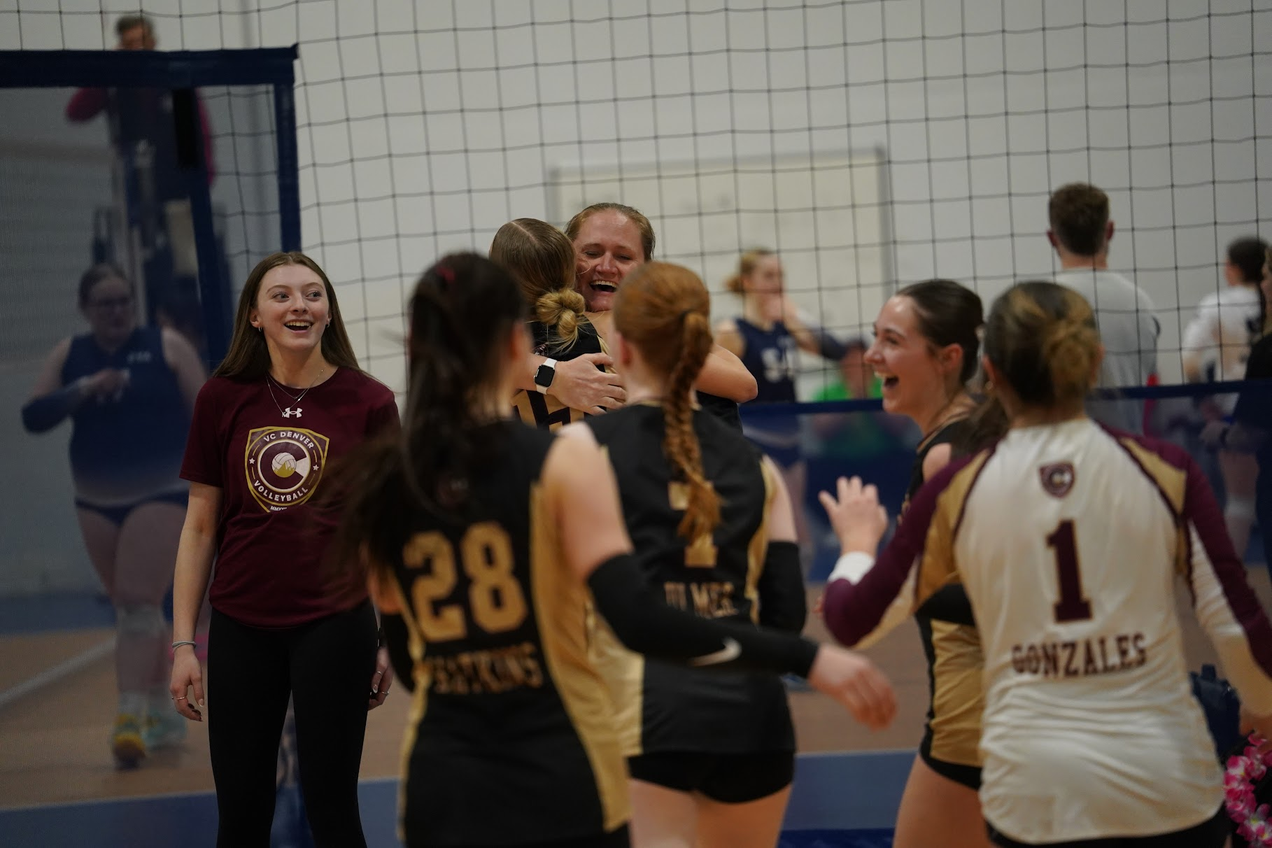 Volleyball players celebrate a point on an indoor court, with hands raised and smiles.