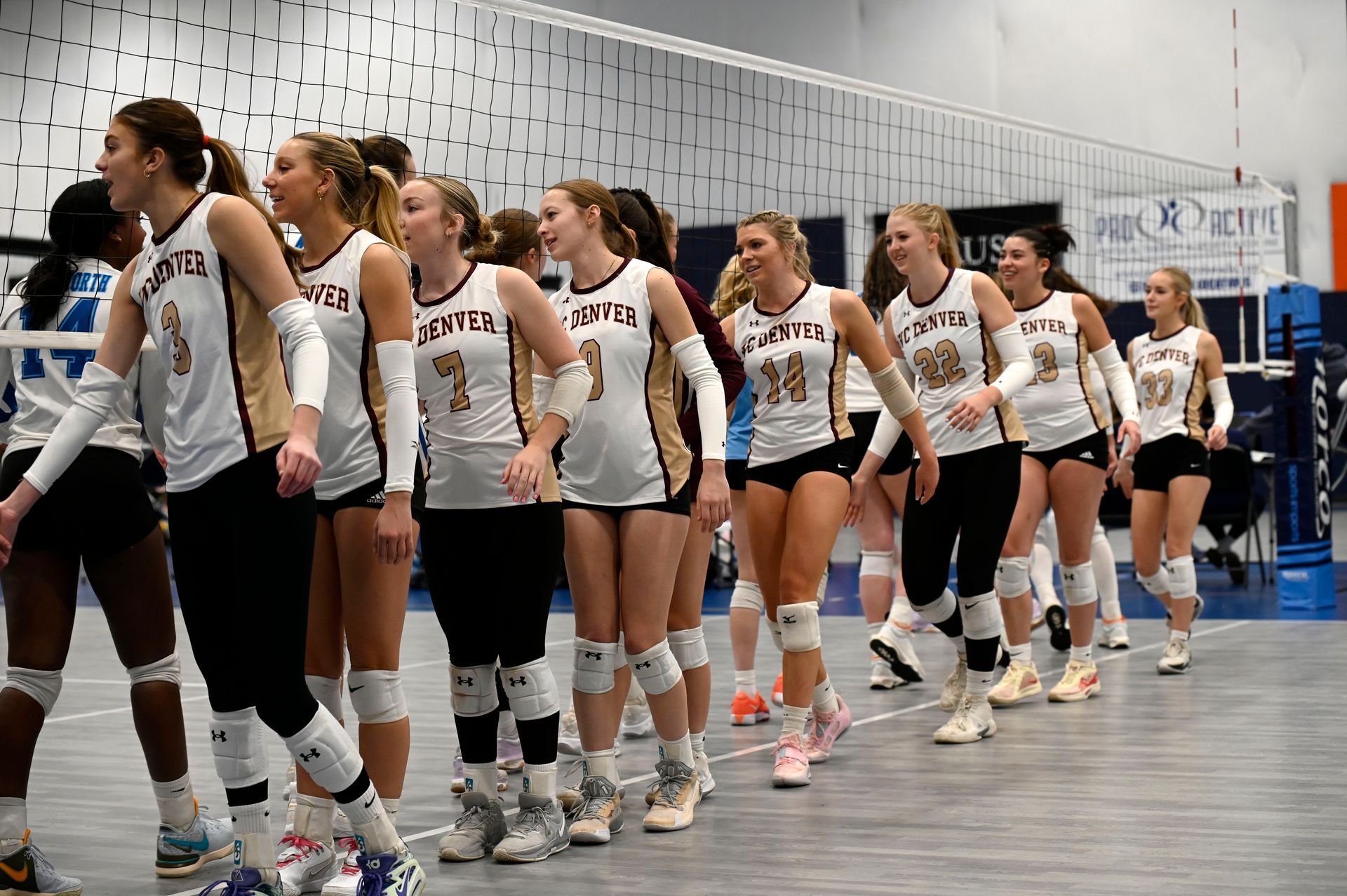 Volleyball team in white uniforms lined up indoors after a match, shaking hands with opponents