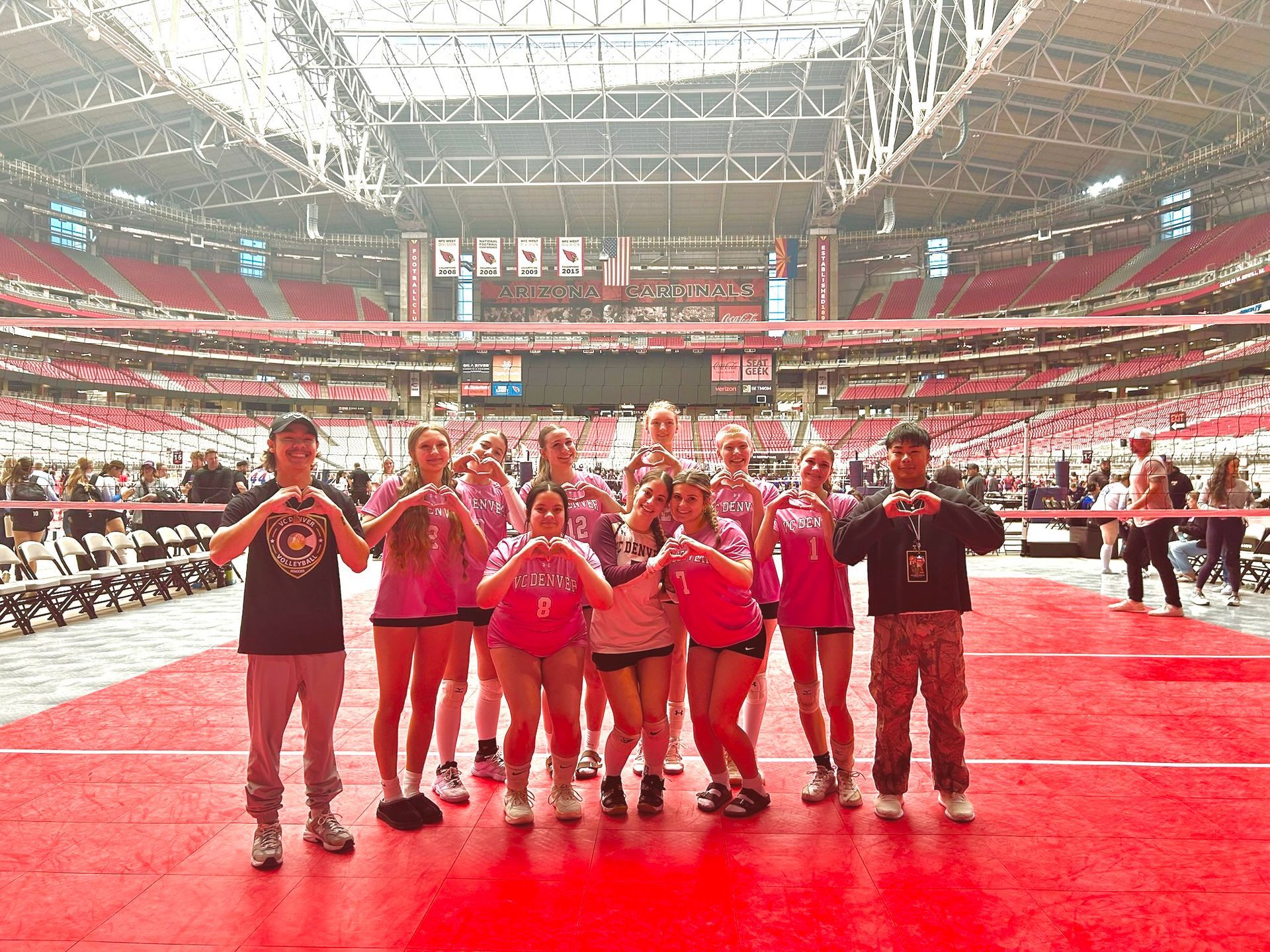 Group of performers in red and black outfits posing on a stadium field with a large crowd in the background