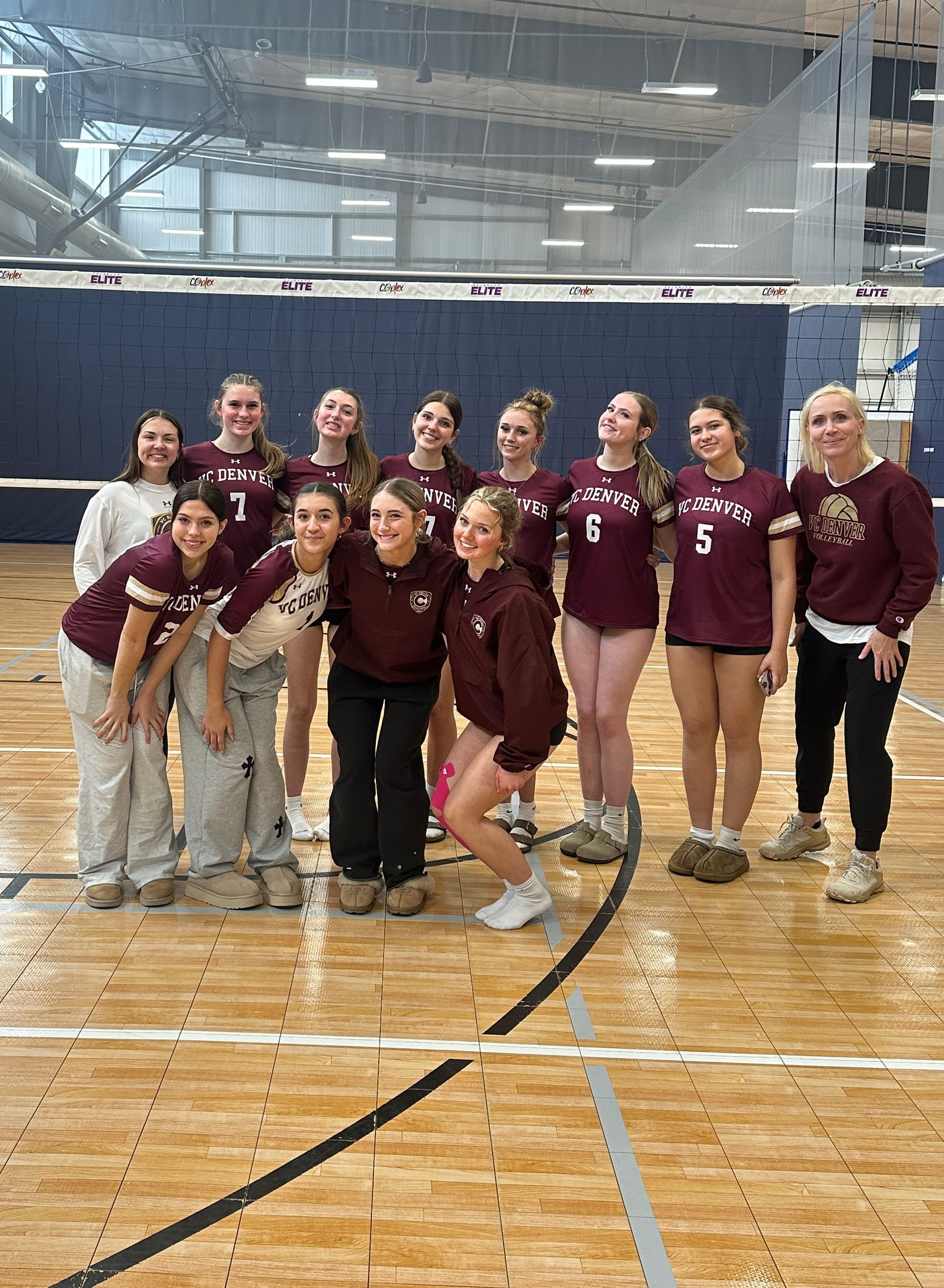 Group of people in maroon shirts posing on an indoor gym court, smiling at the camera.