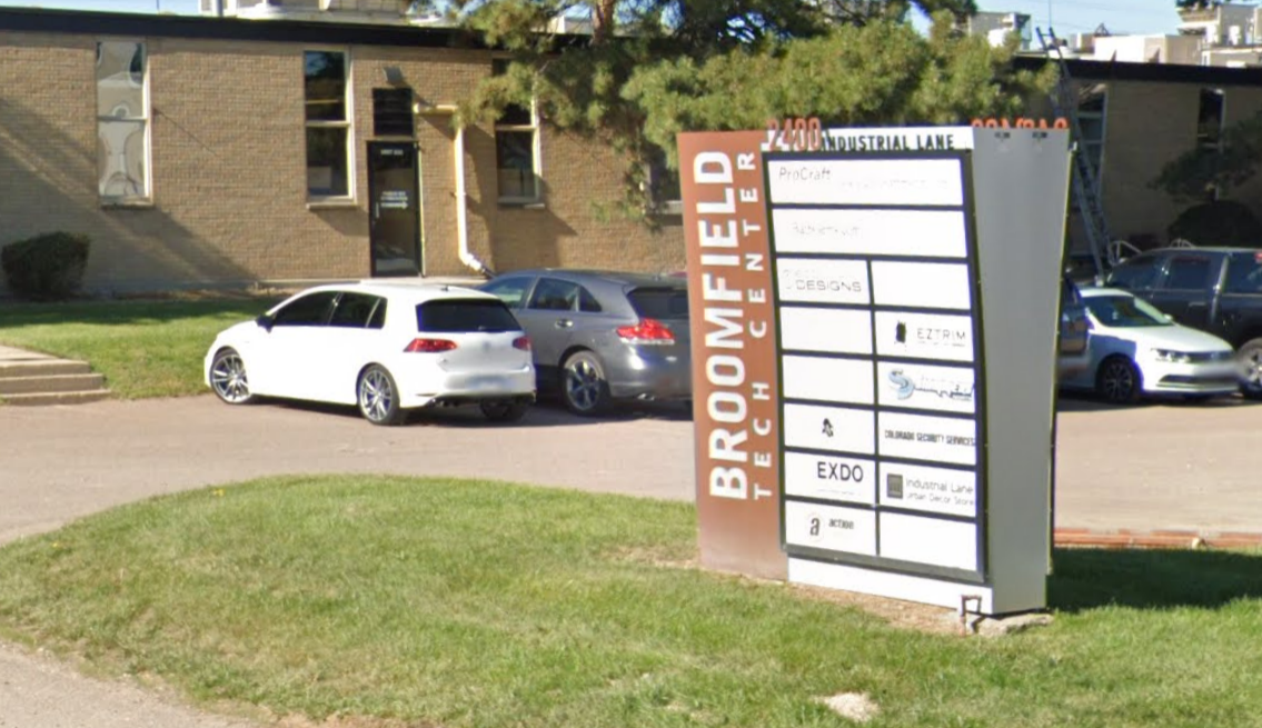 Sign for Broomfield Tech Center with car parking in front of a two-story building.