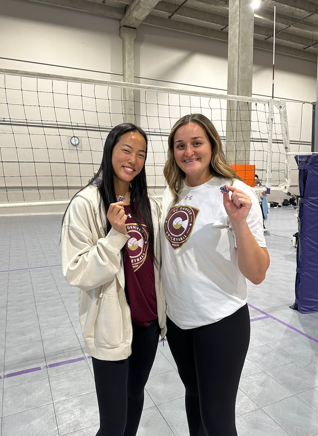 Two people smiling and posing indoors, wearing matching maroon shirts in a large warehouse-like space.