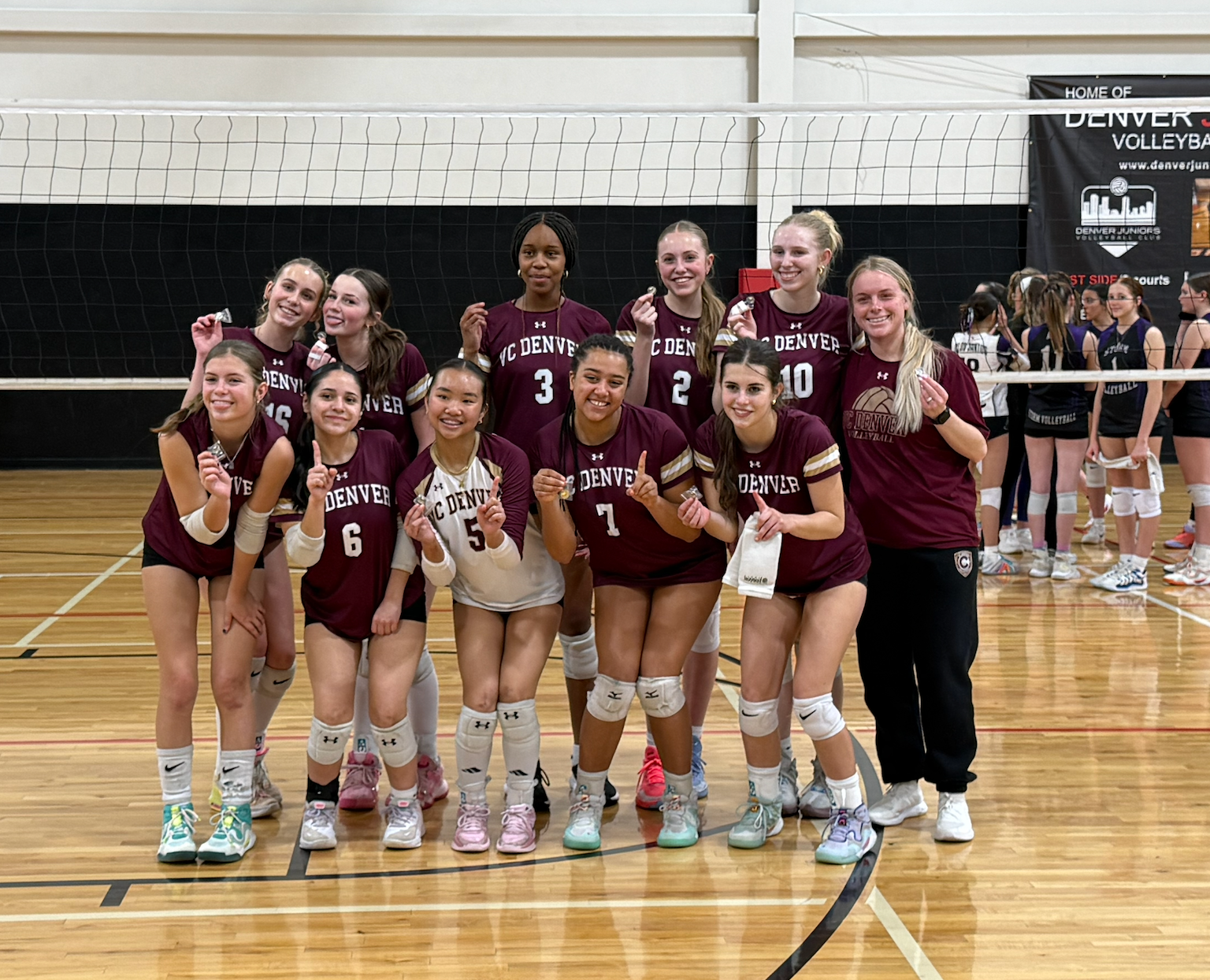 Volleyball team in maroon jerseys posing for a group photo on an indoor court after a match