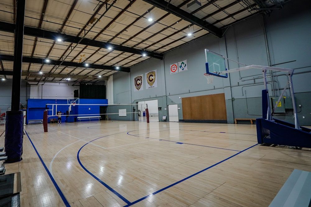 Empty indoor gymnasium with volleyball net, basketball hoop, and polished wood floor