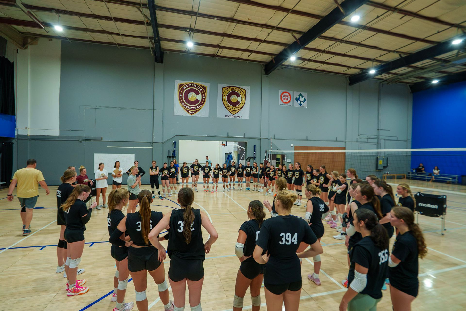 Girls volleyball team posing with ball in gym. Mostly pink shirts.