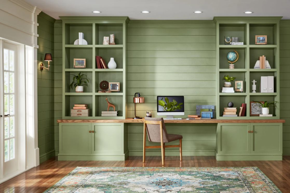 A home office with green walls and shelves and a desk with a computer on it.