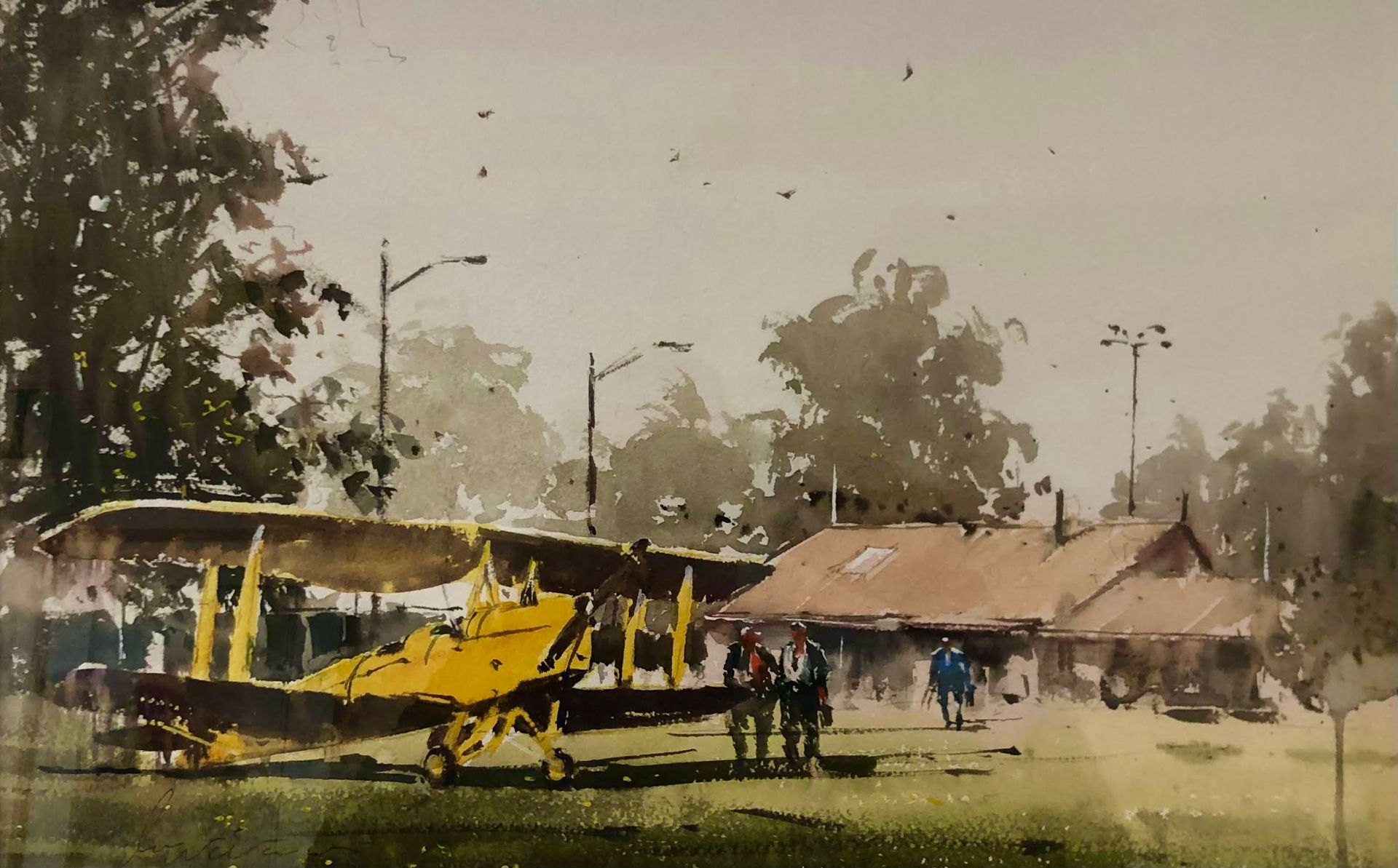 Yellow biplane on a grassy field near huts, with a small group of people standing beside it.