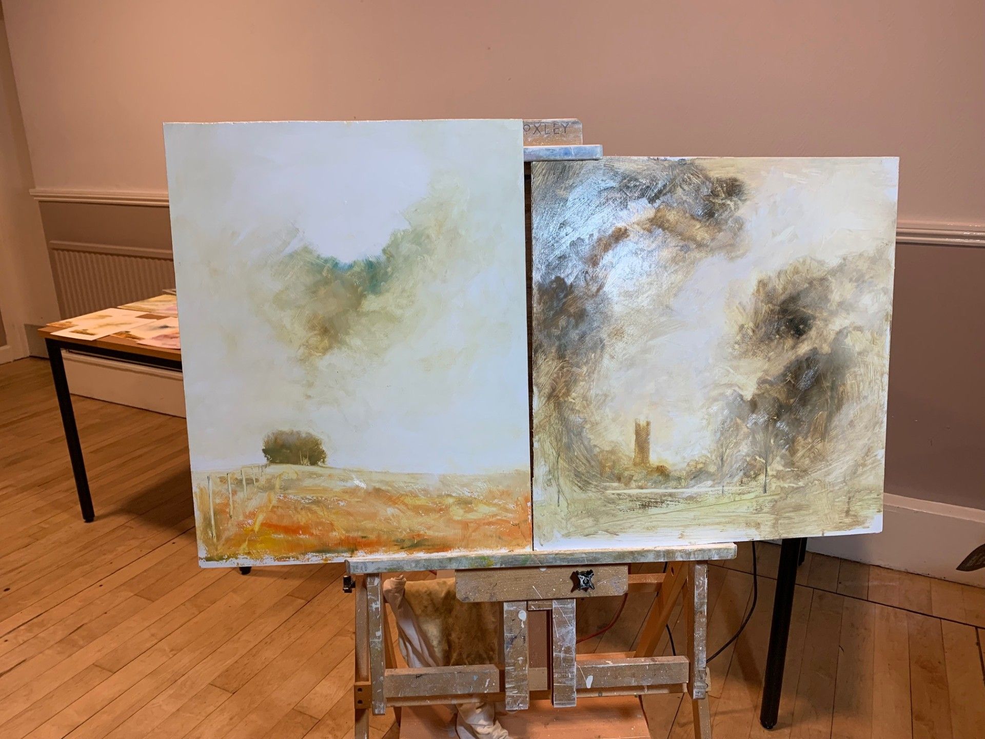 Two abstract landscape paintings on easels in a gallery-like room