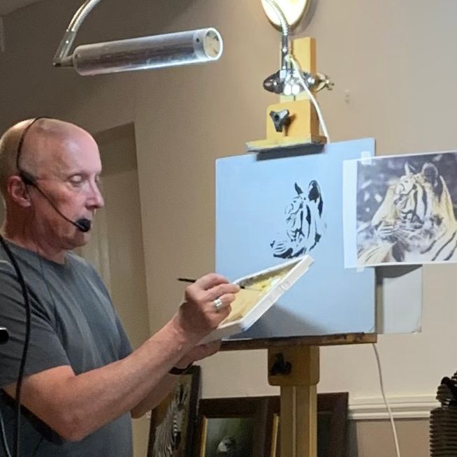 Artist painting on an easel while wearing a headset, with reference sketches nearby.