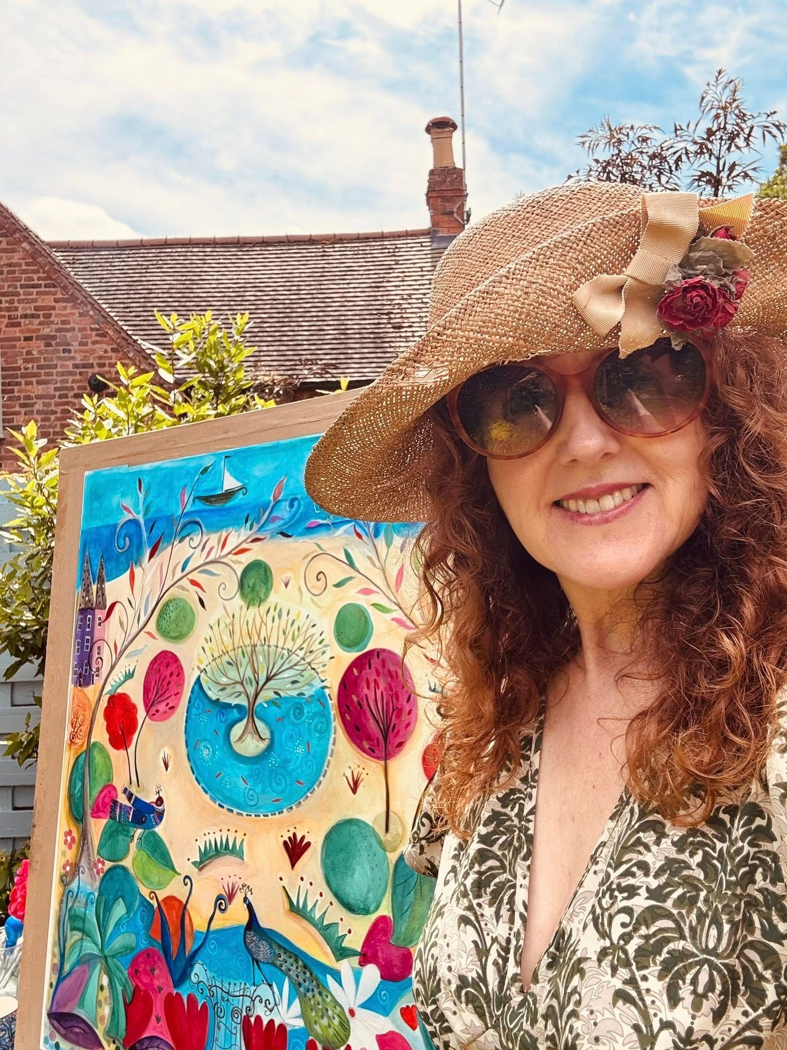 Woman in sunglasses and straw hat beside a colorful birdhouse in a sunny garden