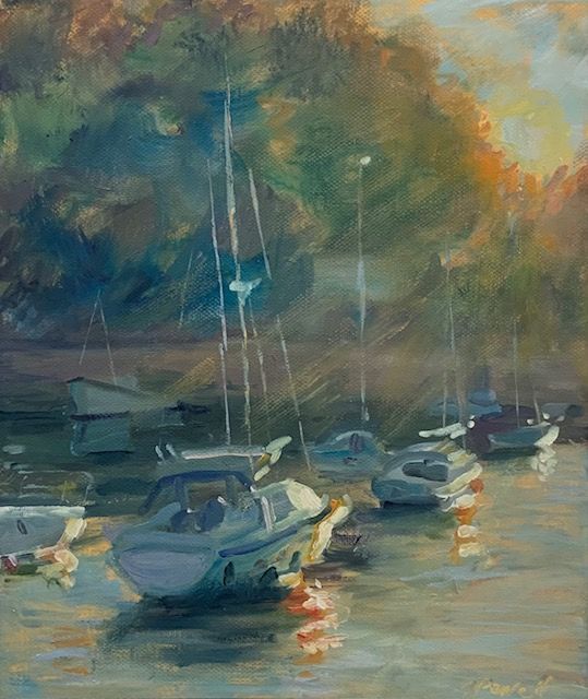 Misty marina with sailboats and small motorboats reflecting on calm water at sunset