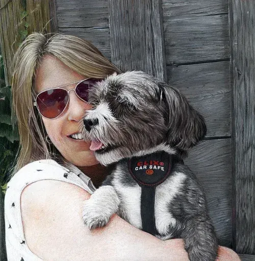 Woman holding a small gray-and-white dog in a harness, both facing the camera against a wooden wall.