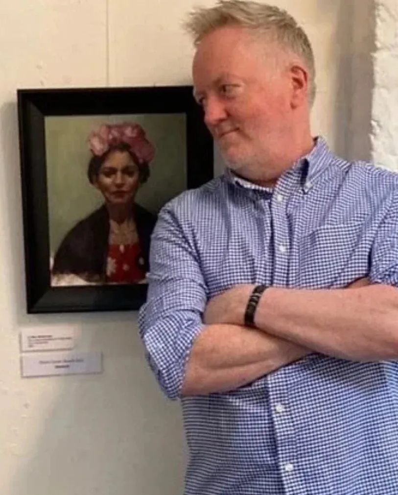 Man standing with arms crossed beside a framed portrait on a gallery wall