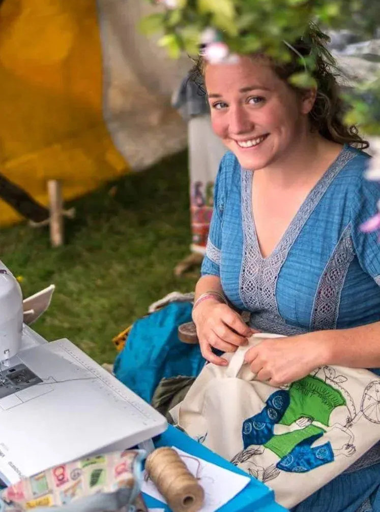 Smiling woman sewing fabric outdoors at a table with a sewing machine and craft supplies